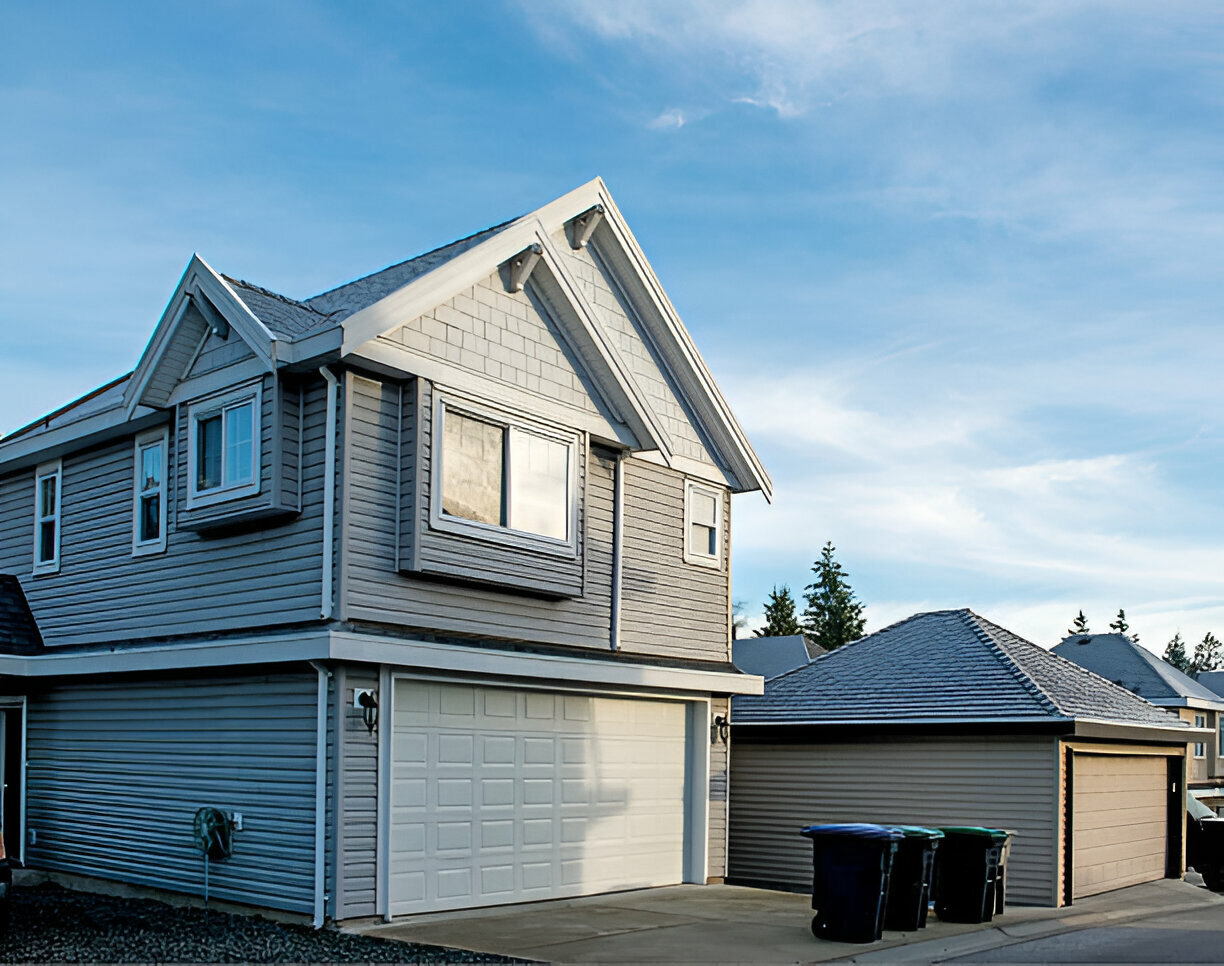 
Modern two-story home with gray siding and a white double garage under a blue sky