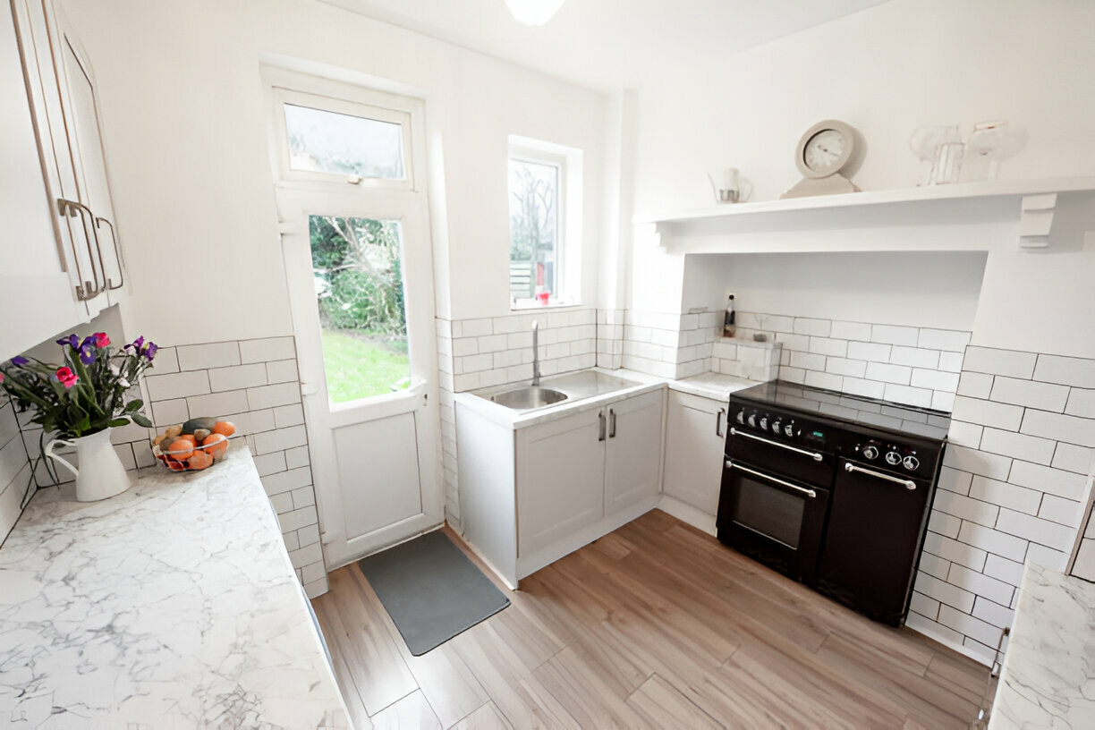 Bright compact kitchen with white subway tile backsplash, marble countertops, and wooden flooring
