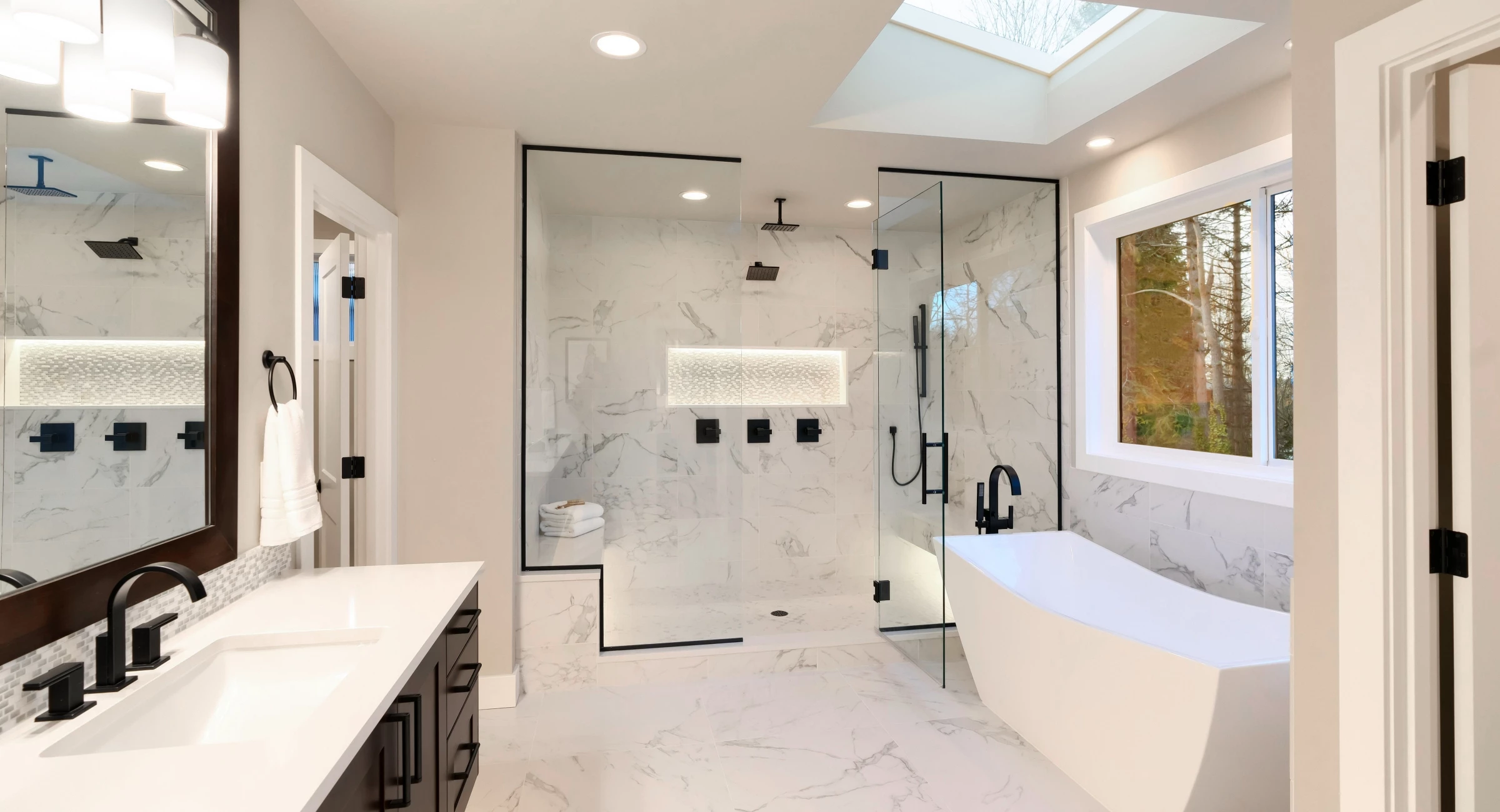 Bright modern bathroom featuring a walk-in glass shower, freestanding soaking tub, black matte fixtures, and marble-look tiles