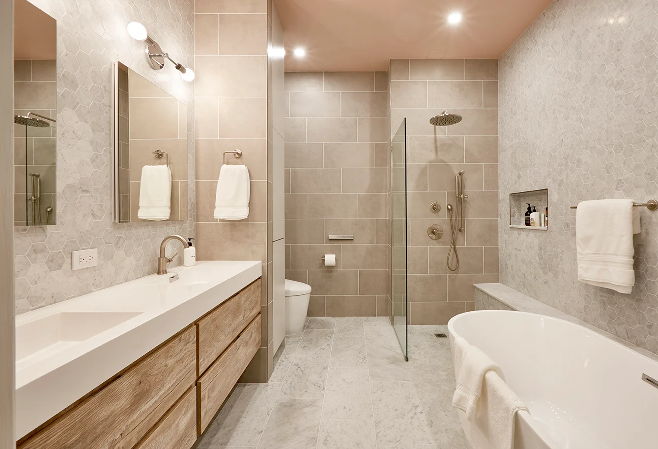 Elegant bathroom featuring a glass walk-in shower, freestanding bathtub, floating wood vanity, and hexagon wall tiles