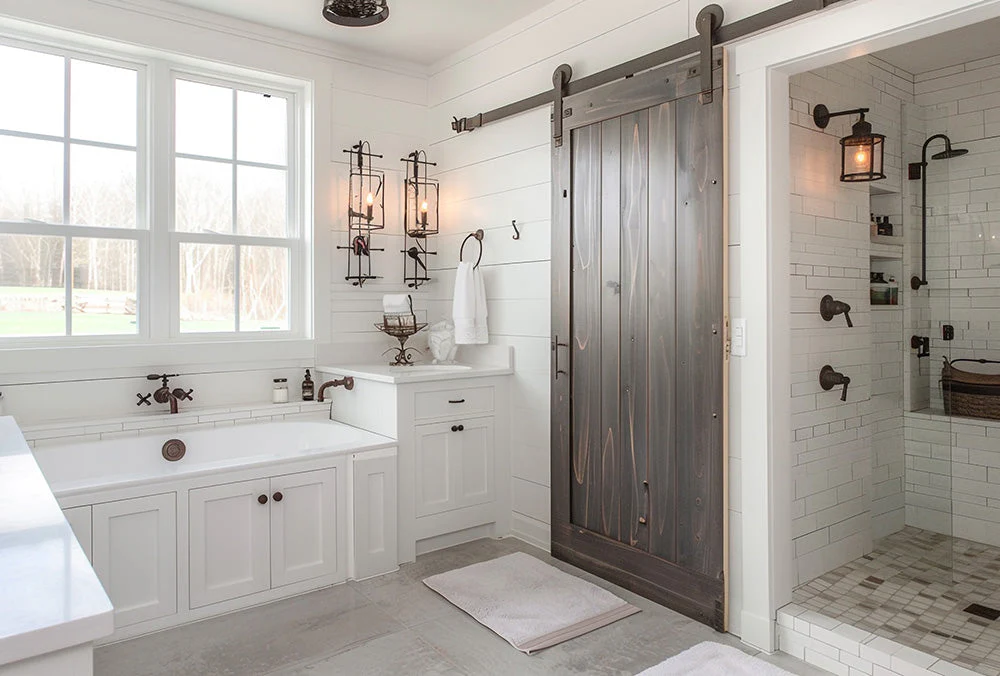 Farmhouse-style bathroom with white shiplap walls, sliding wood barn door, deep soaking tub, and tiled walk-in shower