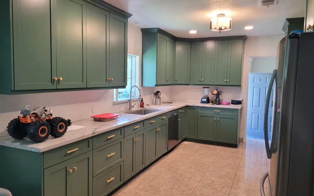 Modern kitchen featuring green shaker-style cabinets with gold handles, white countertops, and tile flooring