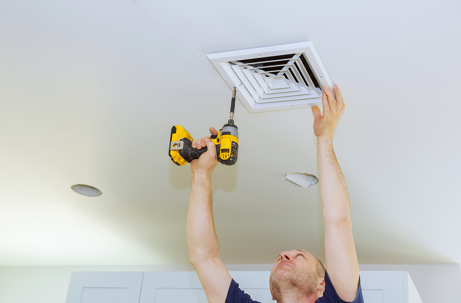 Technician using a power drill to install a ventilation grille on a bathroom ceiling