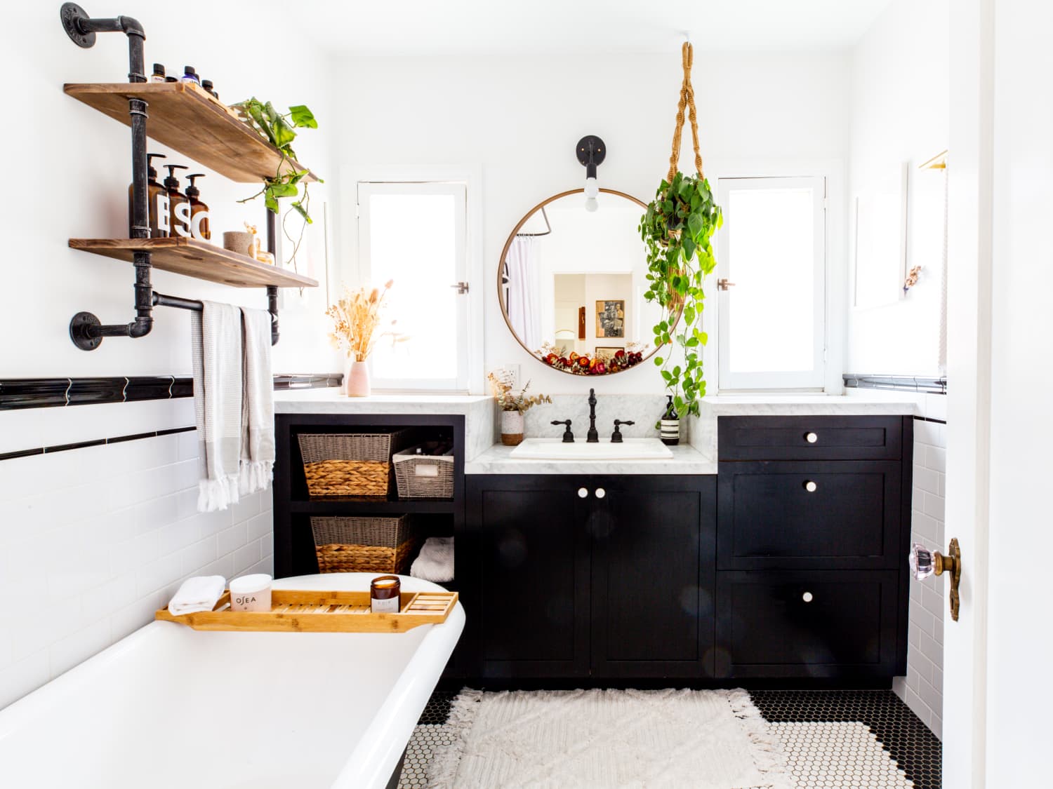 Farmhouse-style bathroom featuring a black vanity, round mirror, hanging plant, and rustic wooden shelves