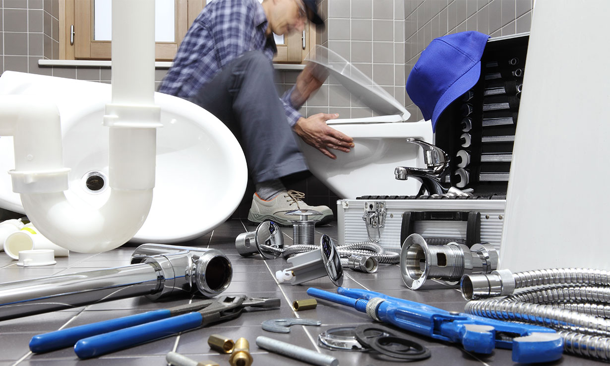 Plumber installing toilet in a modern bathroom surrounded by plumbing tools and fixtures