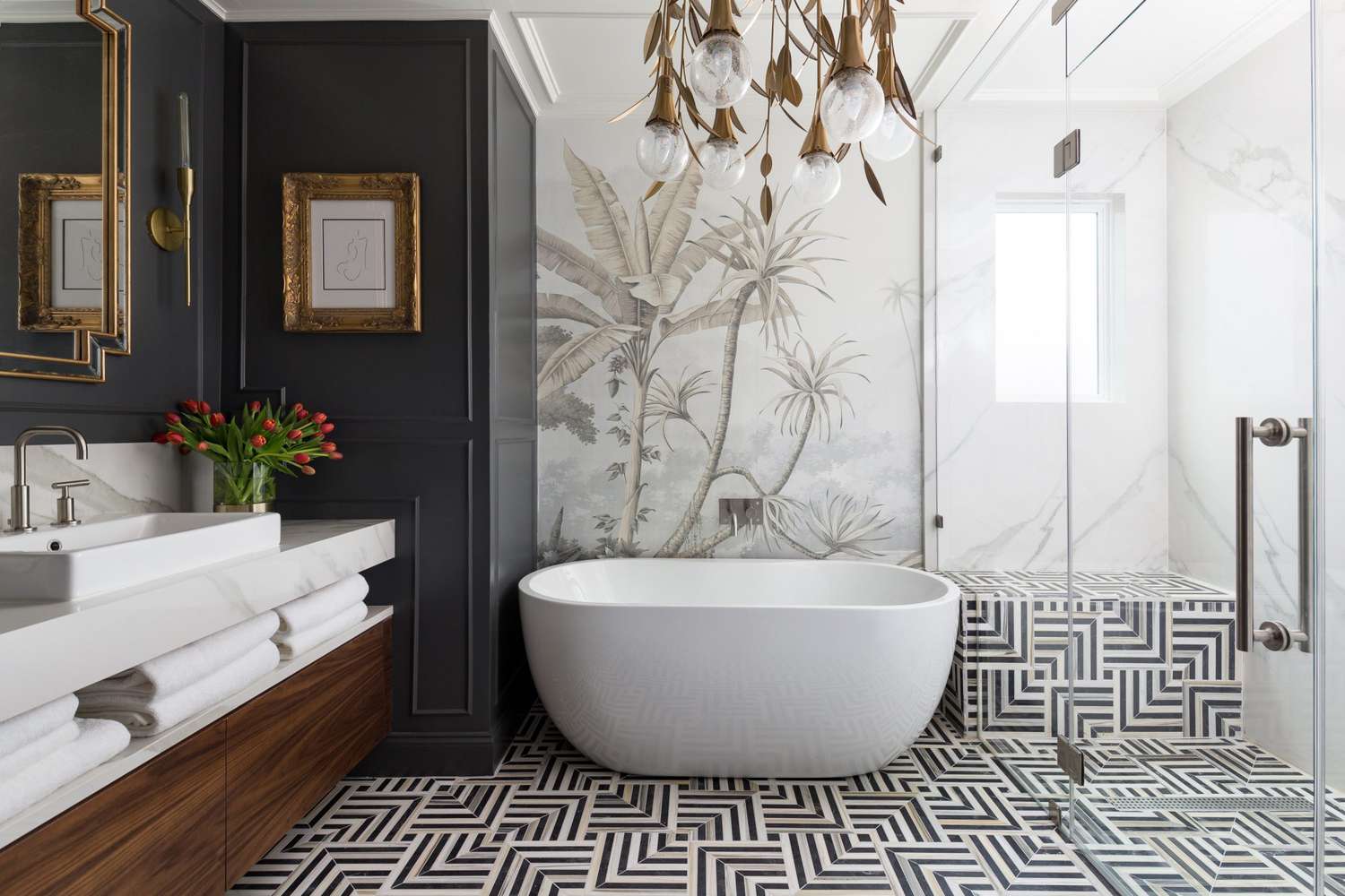 Elegant bathroom featuring a freestanding white tub, botanical wall mural, geometric tile flooring, and brass lighting fixtures