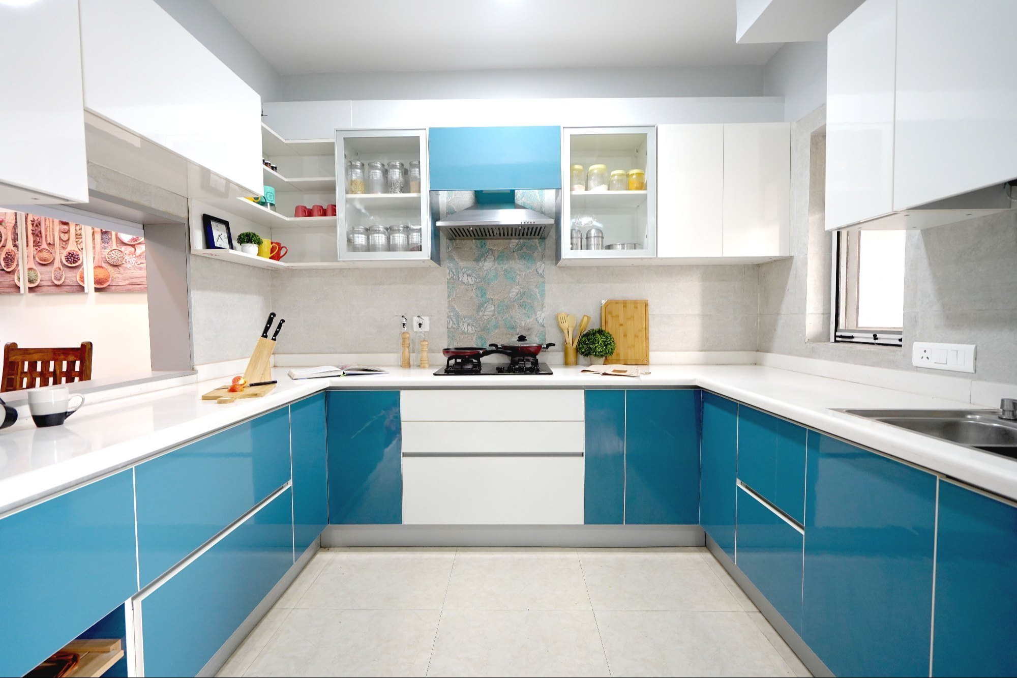 U-shaped modular kitchen with glossy blue and white cabinets, sleek white countertops, and open shelving