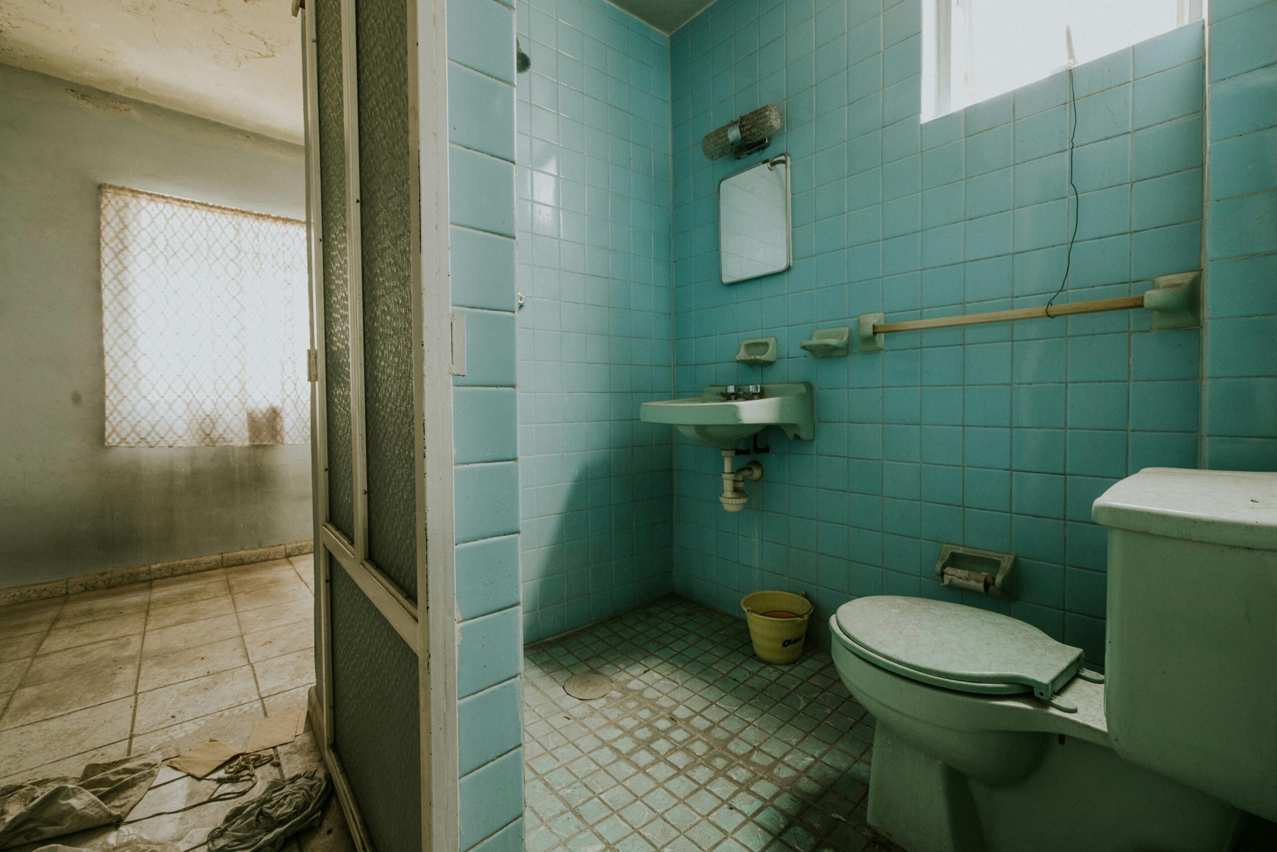 Old bathroom with faded blue tiles, wall-mounted sink, and toilet