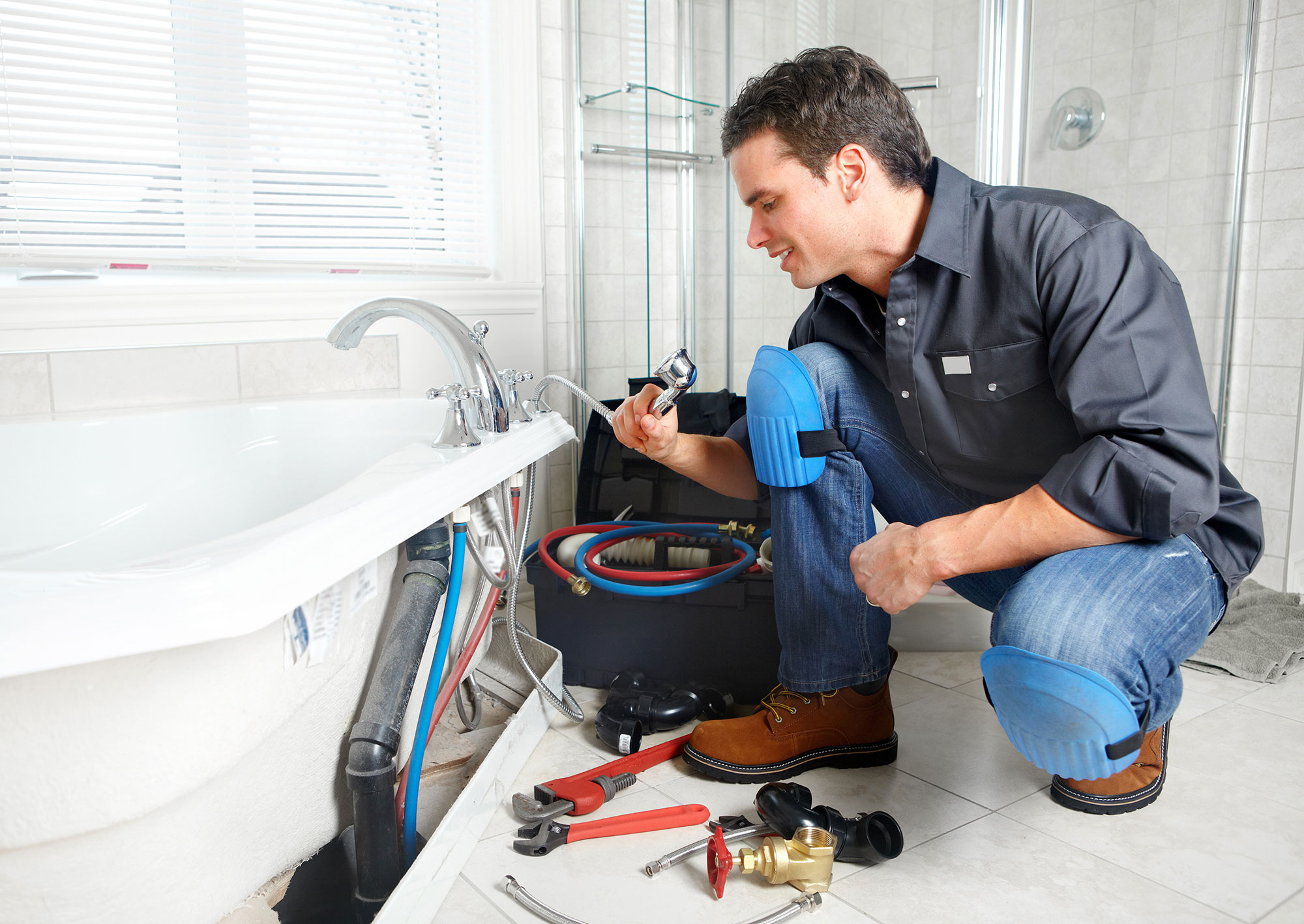 Plumber repairing bathtub plumbing with tools and knee pads in a modern bathroom