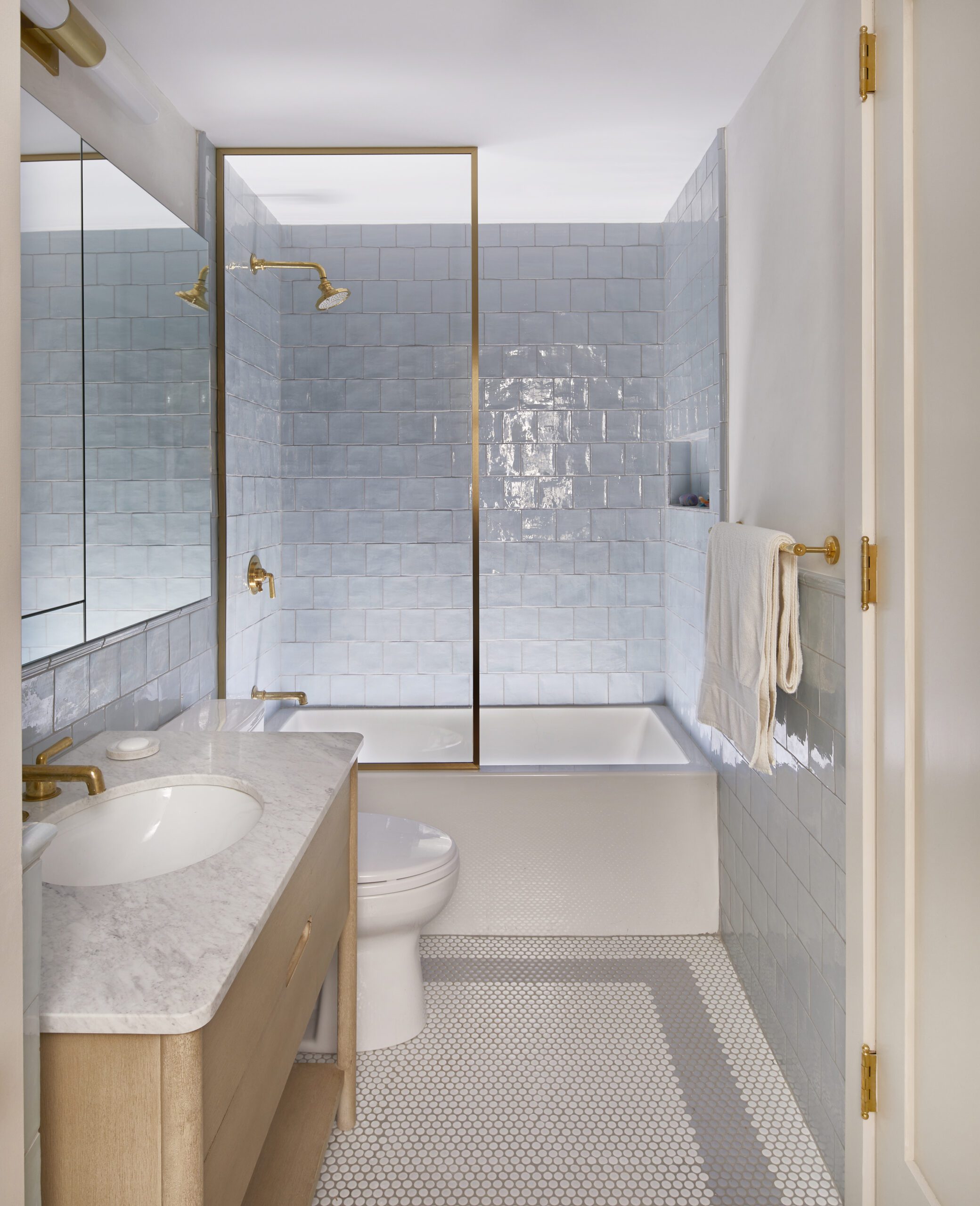 Modern bathroom featuring soft blue square tiles, brass shower fixtures, and a white vanity with marble countertop
