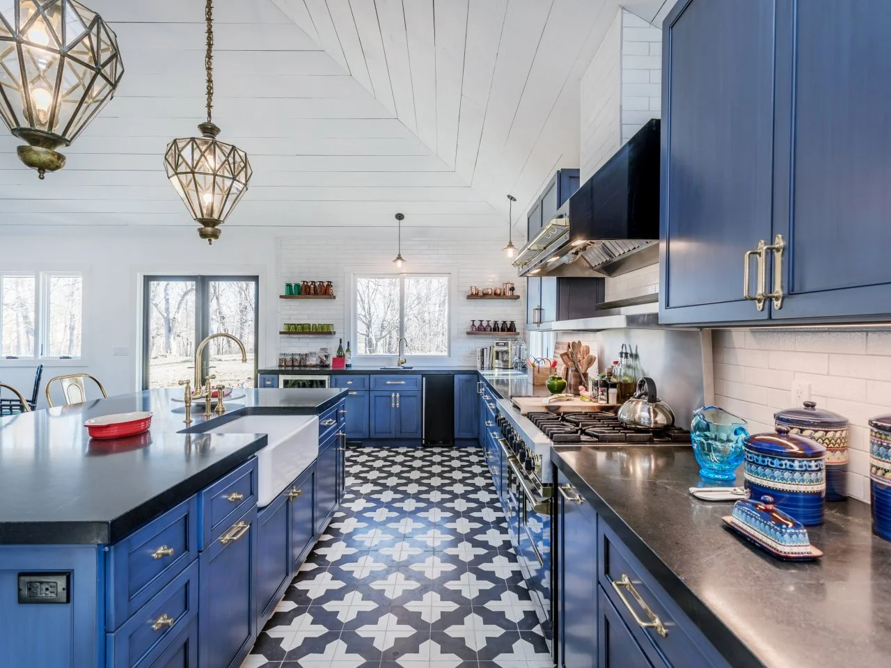 Spacious kitchen featuring navy blue cabinets, black countertops, patterned black and white tile flooring, and stylish pendant lights.
