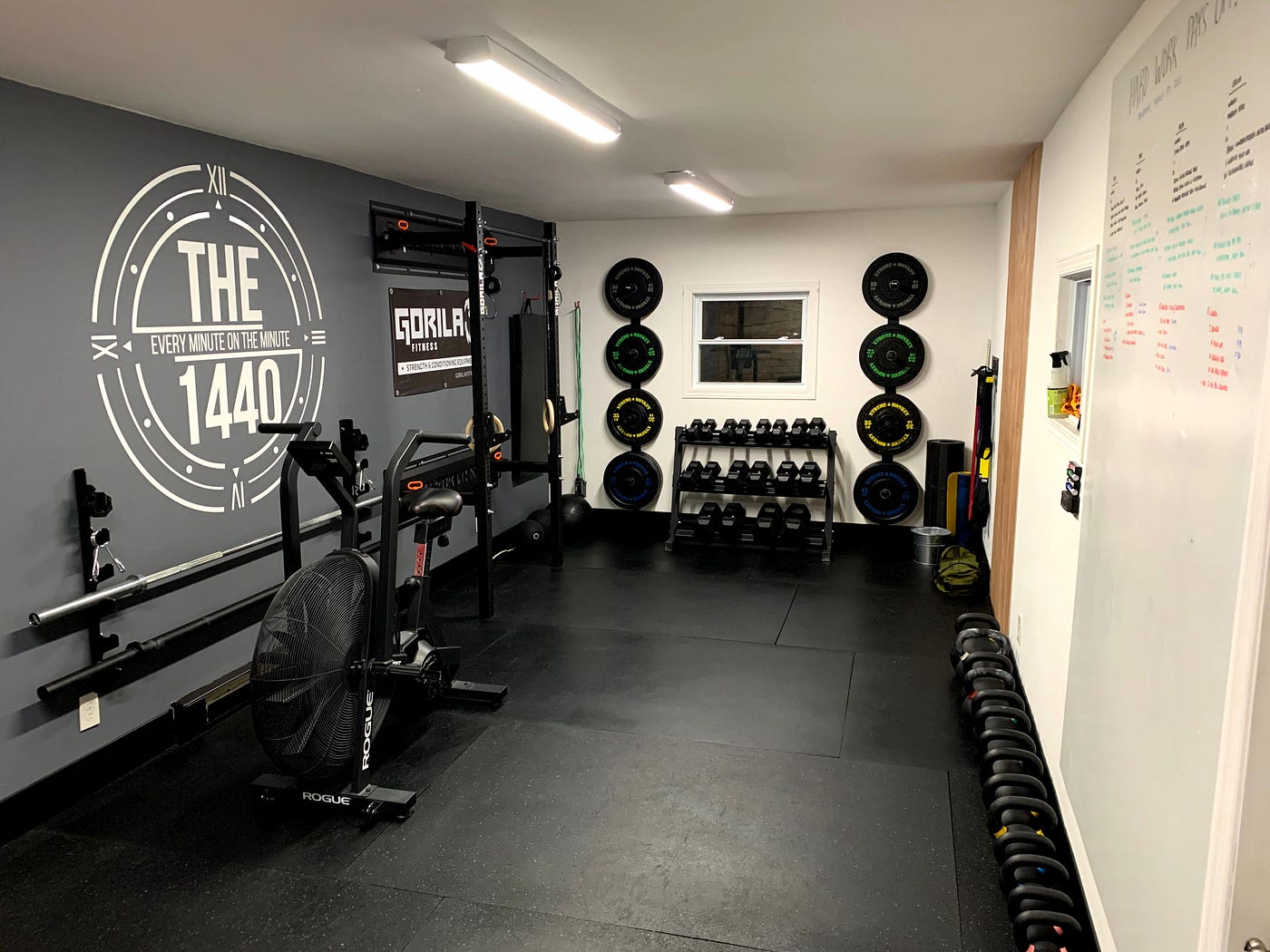 Home gym with wall-mounted weights, dumbbells, exercise bike, rubber flooring, and motivational wall decor.
