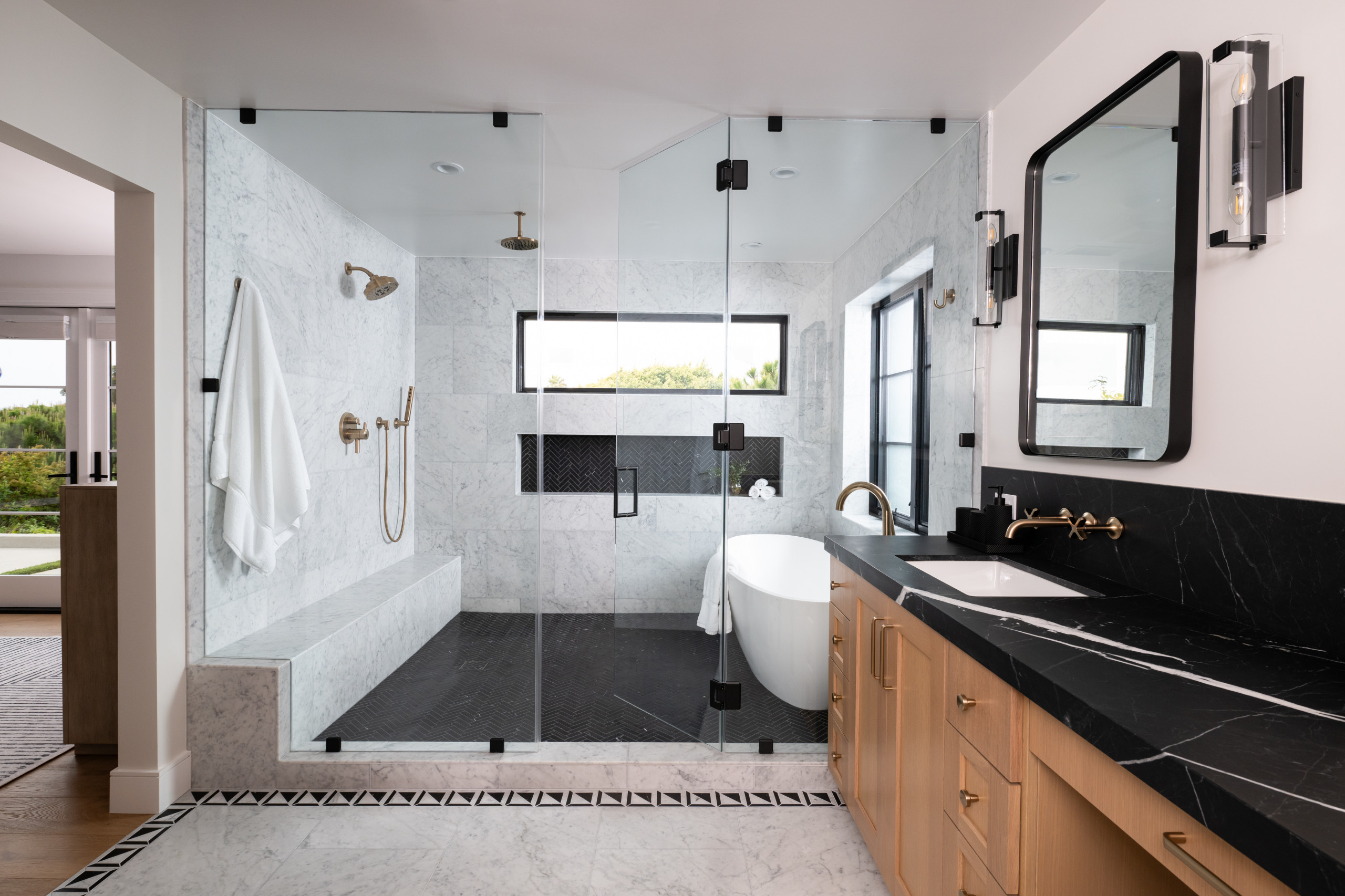 Luxury bathroom with glass shower, freestanding bathtub, and black marble countertop