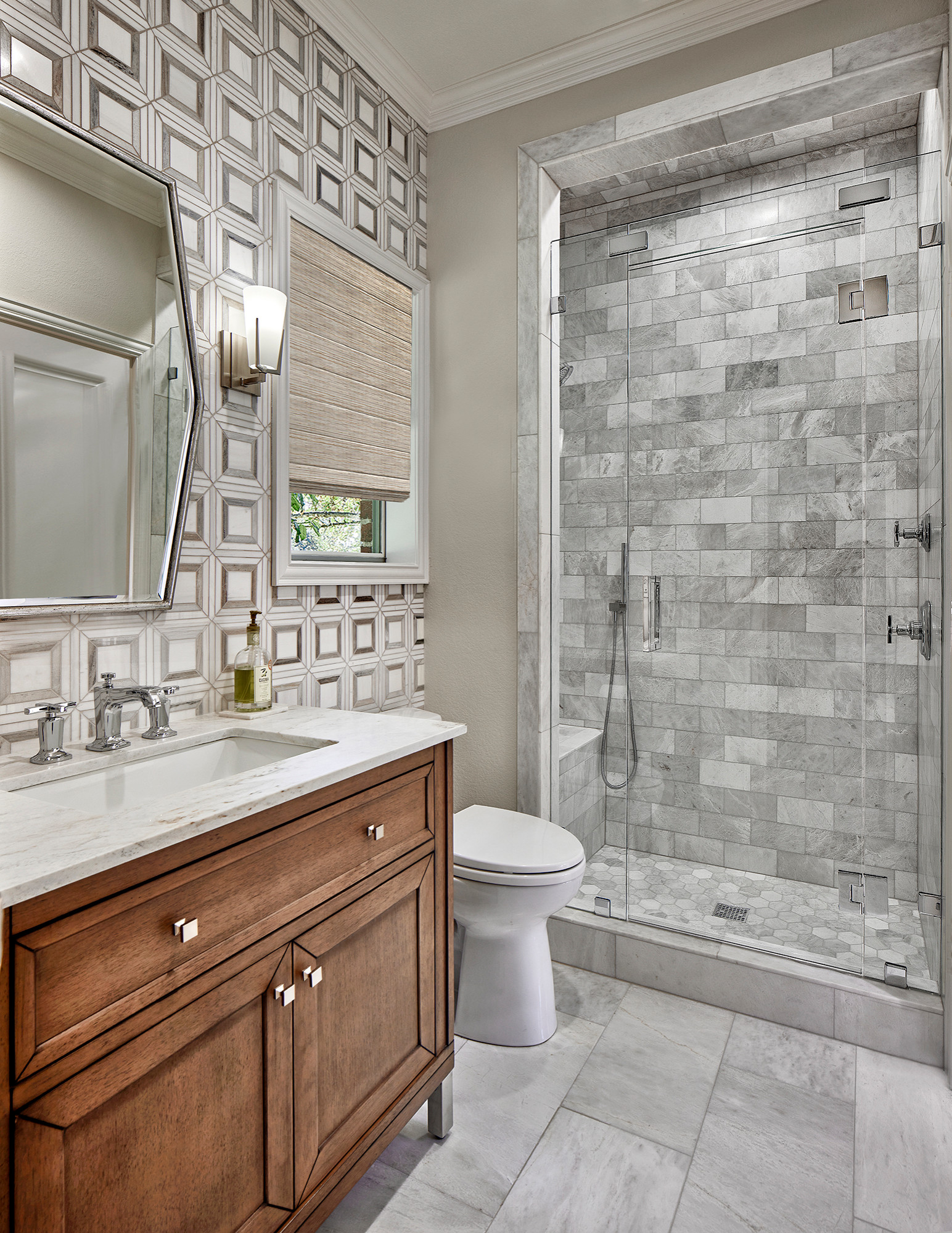 Bathroom with wood vanity, glass shower, and geometric accent wall.