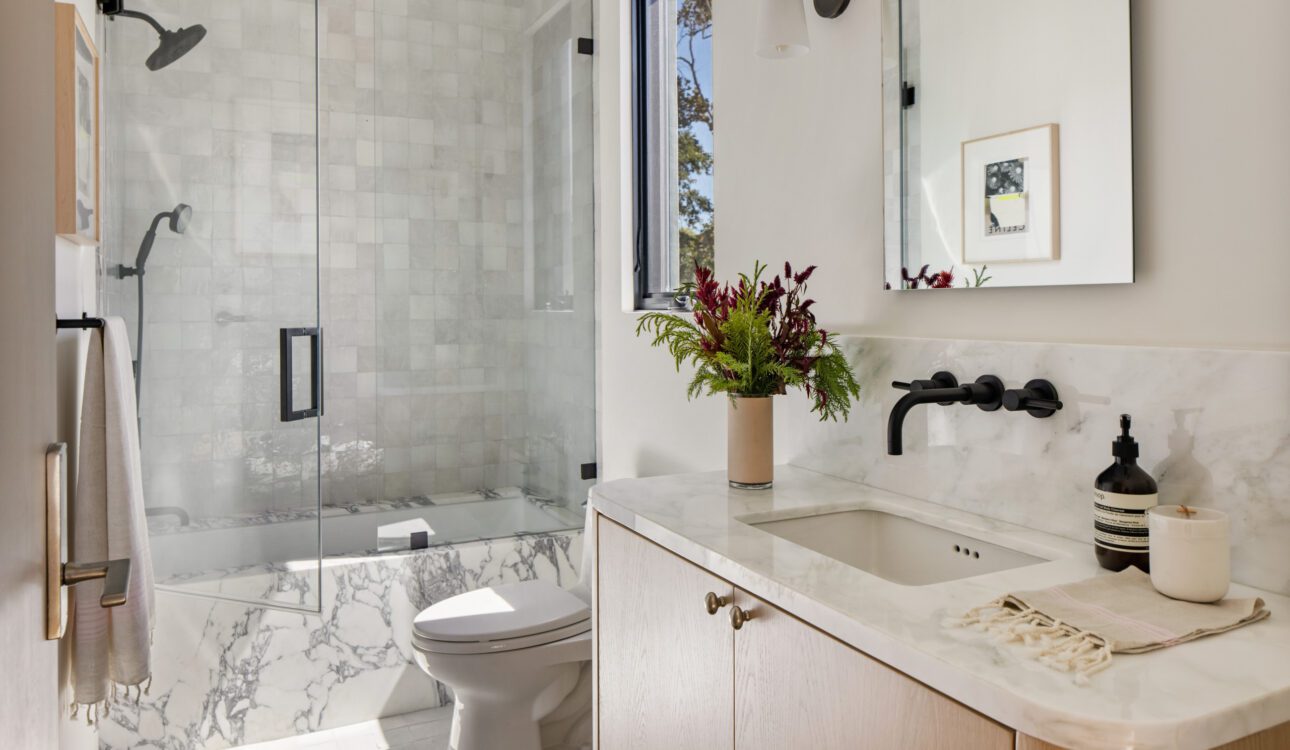Modern bathroom with glass shower, marble tub, and light wood vanity.
