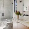 Modern bathroom with glass shower, marble tub, and light wood vanity.