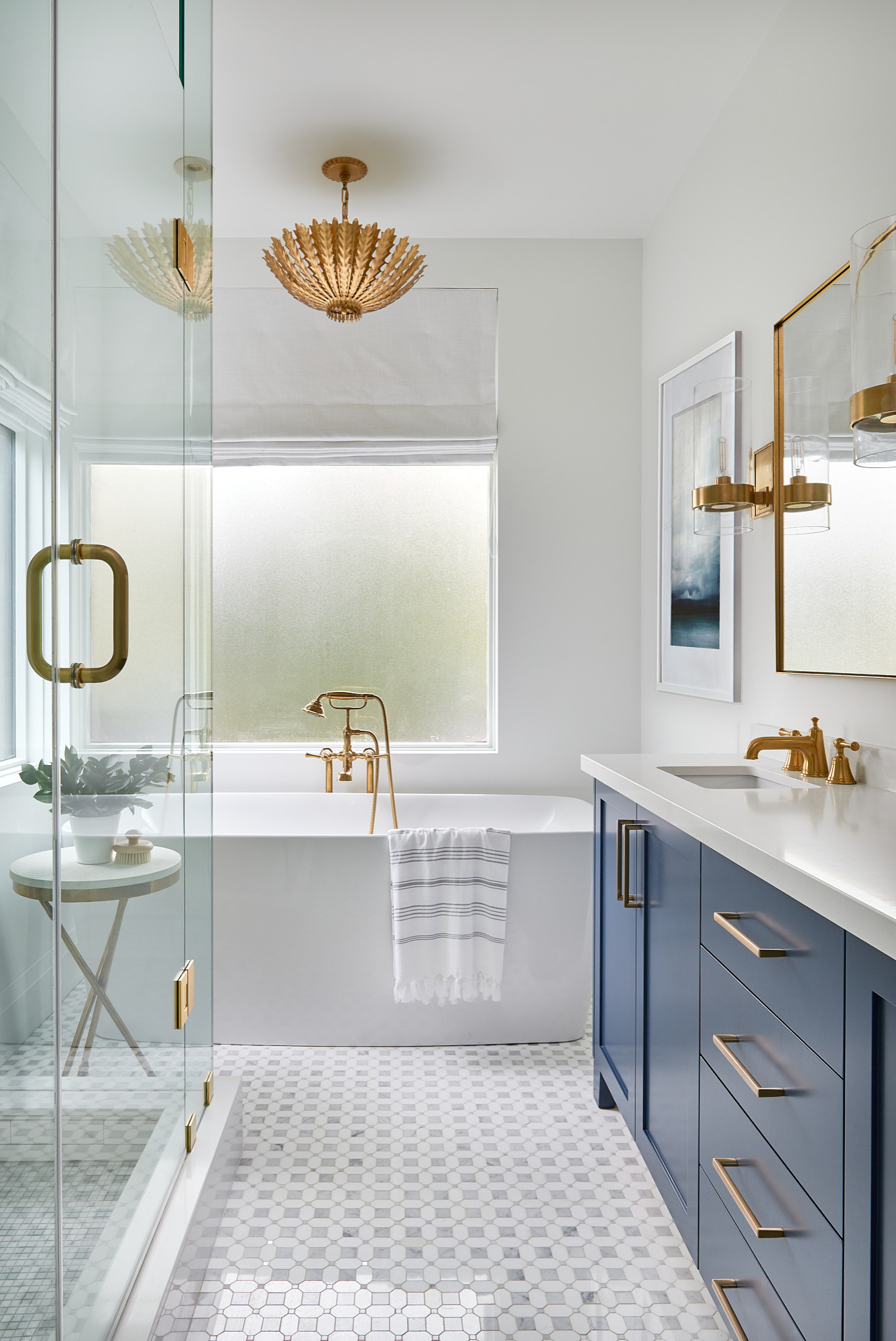 Modern bathroom with blue vanity, freestanding tub, and gold fixtures.
