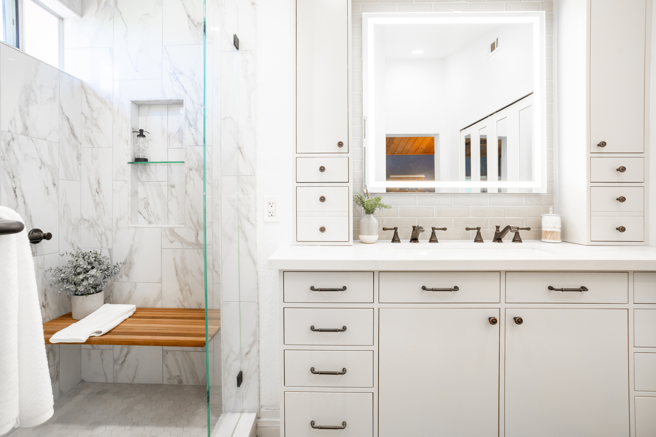 Elegant bathroom with marble shower, built-in bench, light cabinetry, and illuminated vanity mirror.