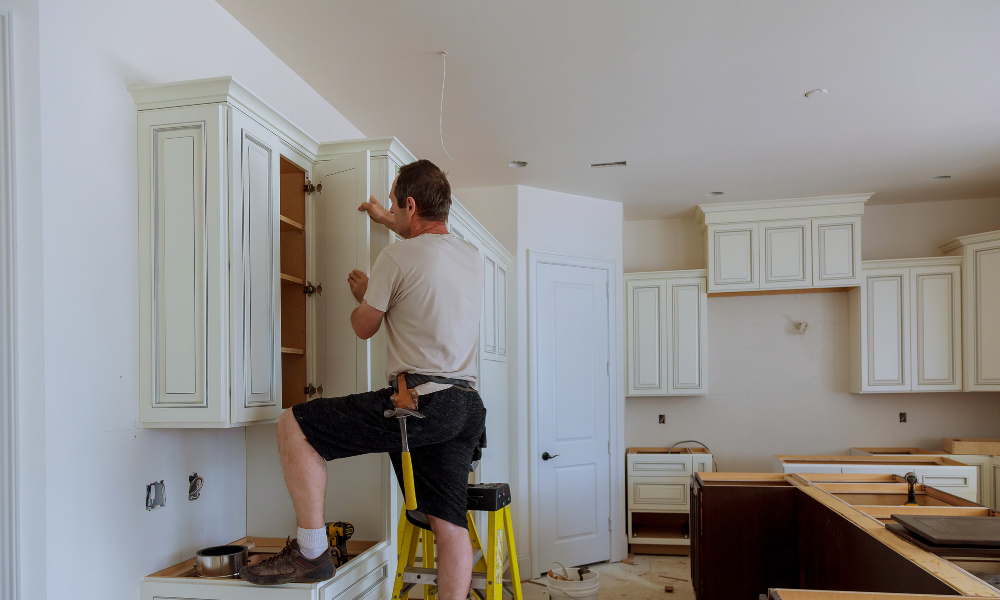 Worker installing upper cabinets during a kitchen remodeling project.