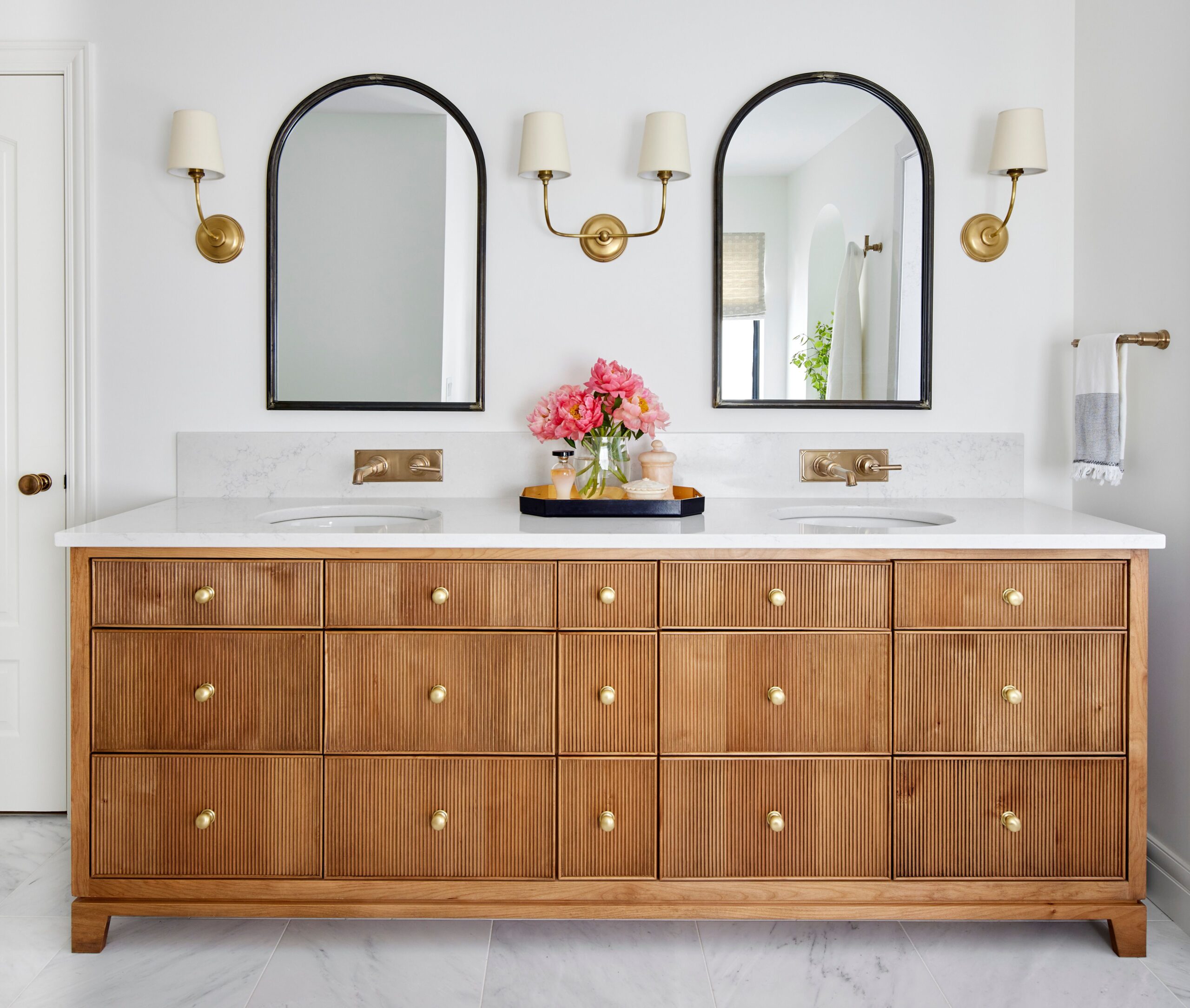 Wooden double vanity with marble countertop, gold fixtures, and arched mirrors