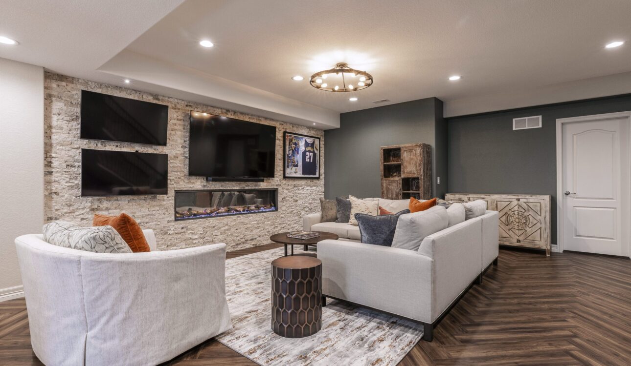 A stylish basement living room featuring a stone wall with multiple TVs, a modern fireplace, and elegant furniture.