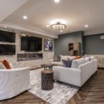 A stylish basement living room featuring a stone wall with multiple TVs, a modern fireplace, and elegant furniture.