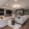A stylish basement living room featuring a stone wall with multiple TVs, a modern fireplace, and elegant furniture.
