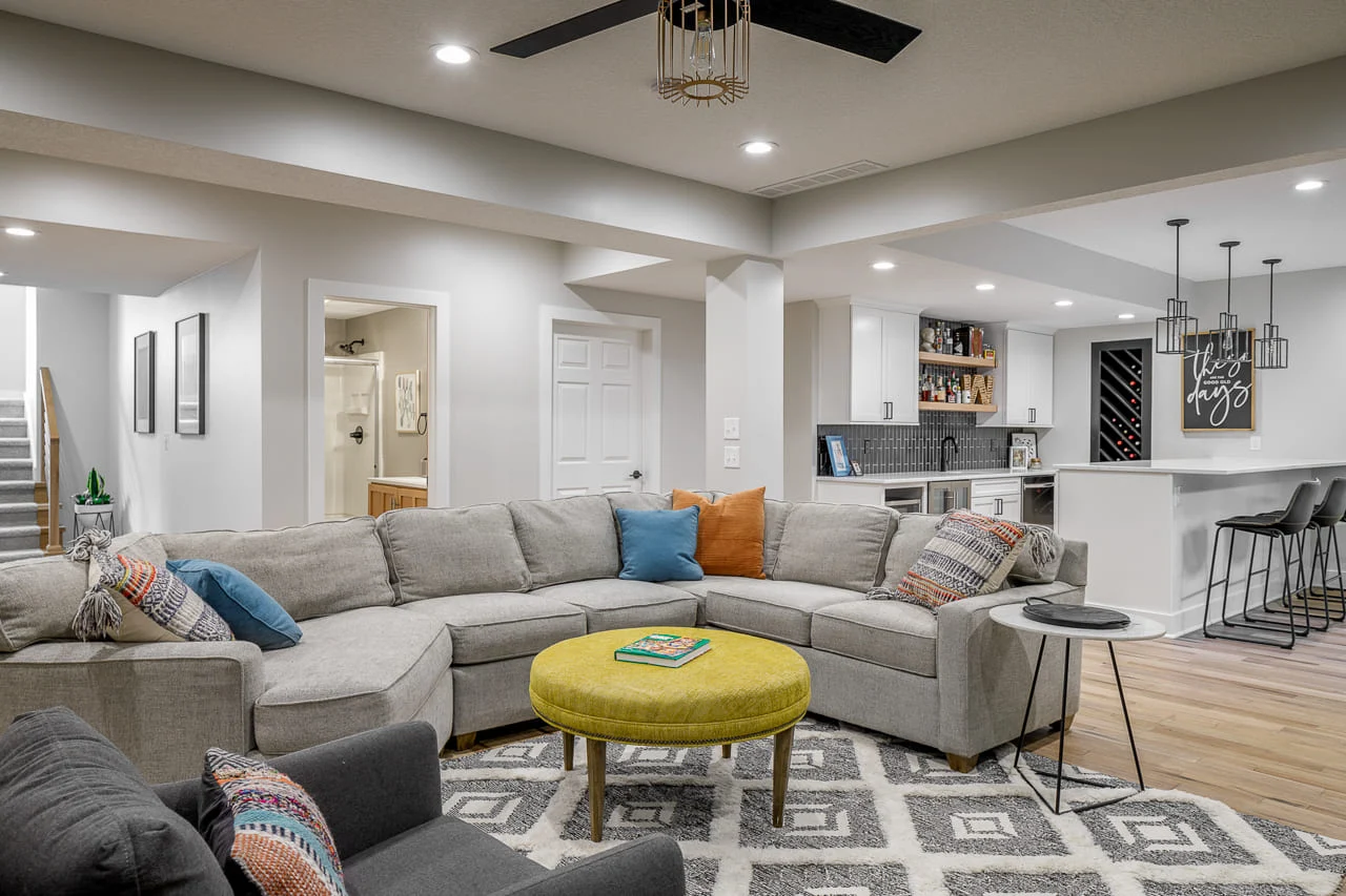 A stylish finished basement featuring a large sectional sofa, wet bar, and modern decor.