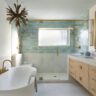 Luxurious bathroom with freestanding bathtub, glass shower, green tiles, and gold fixtures.