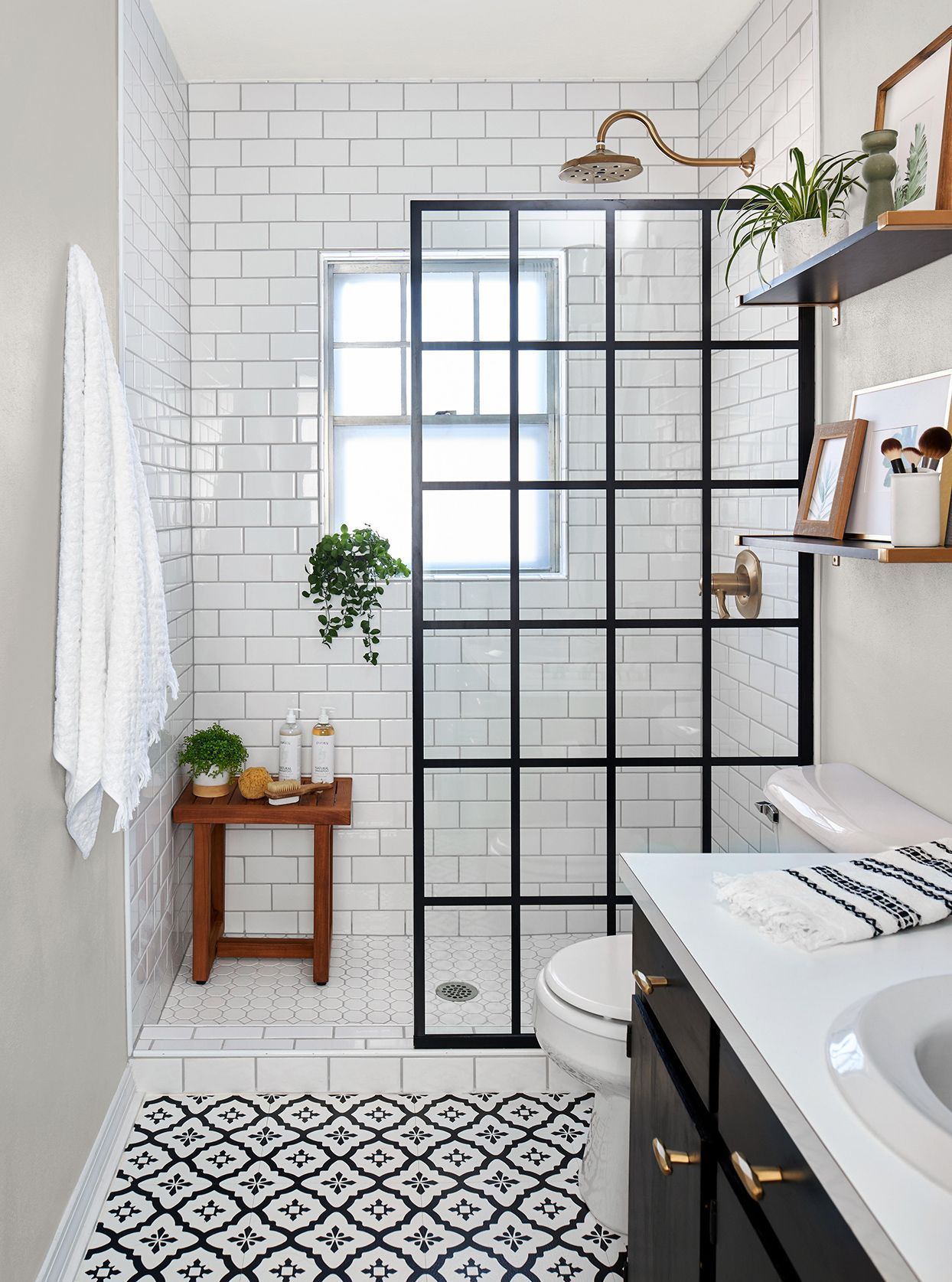 Compact bathroom featuring white subway tiles, a black-framed glass shower partition, patterned black and white floor tiles, and wooden accents.