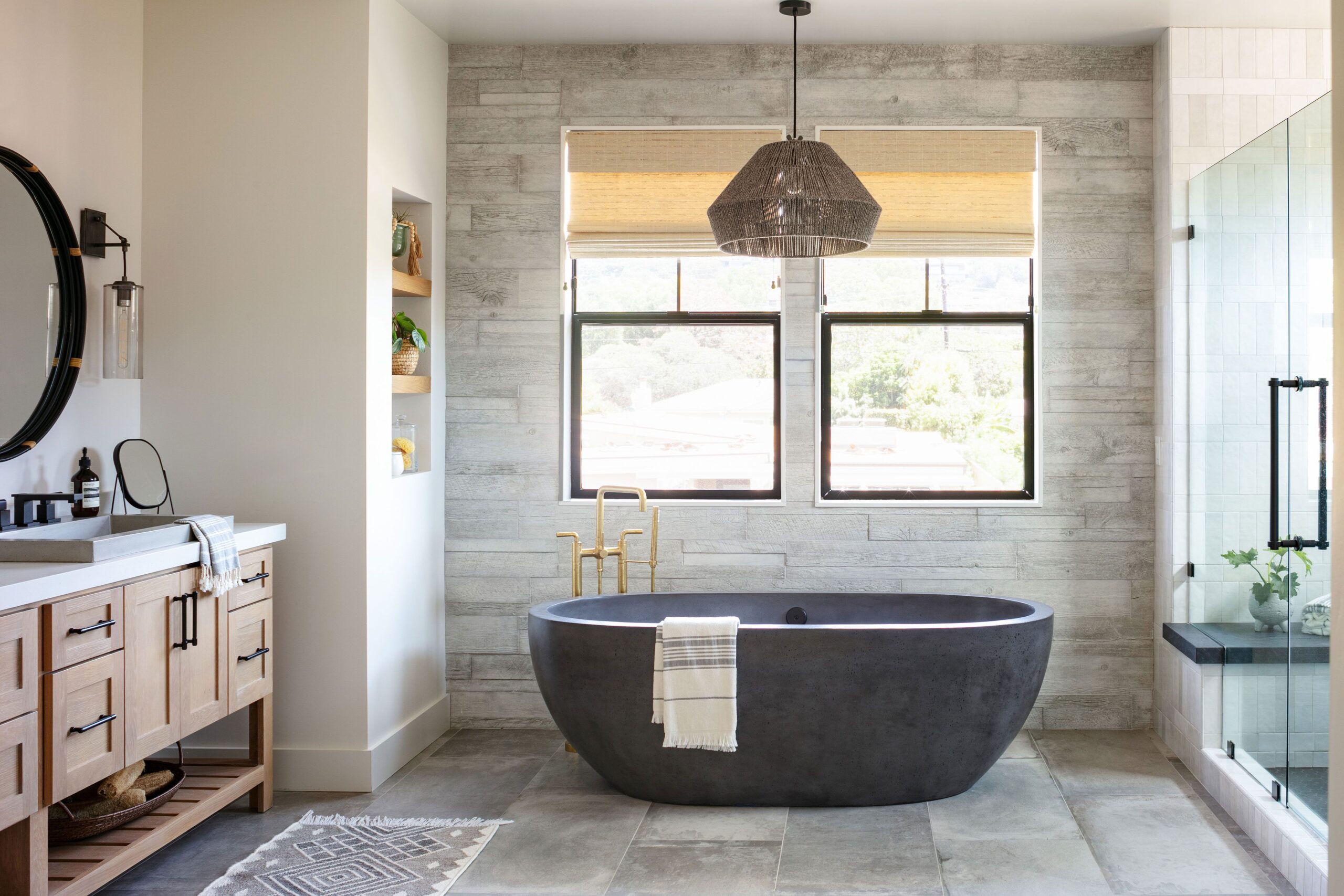 Modern bathroom with a freestanding dark stone bathtub, wooden vanity, and glass shower enclosure