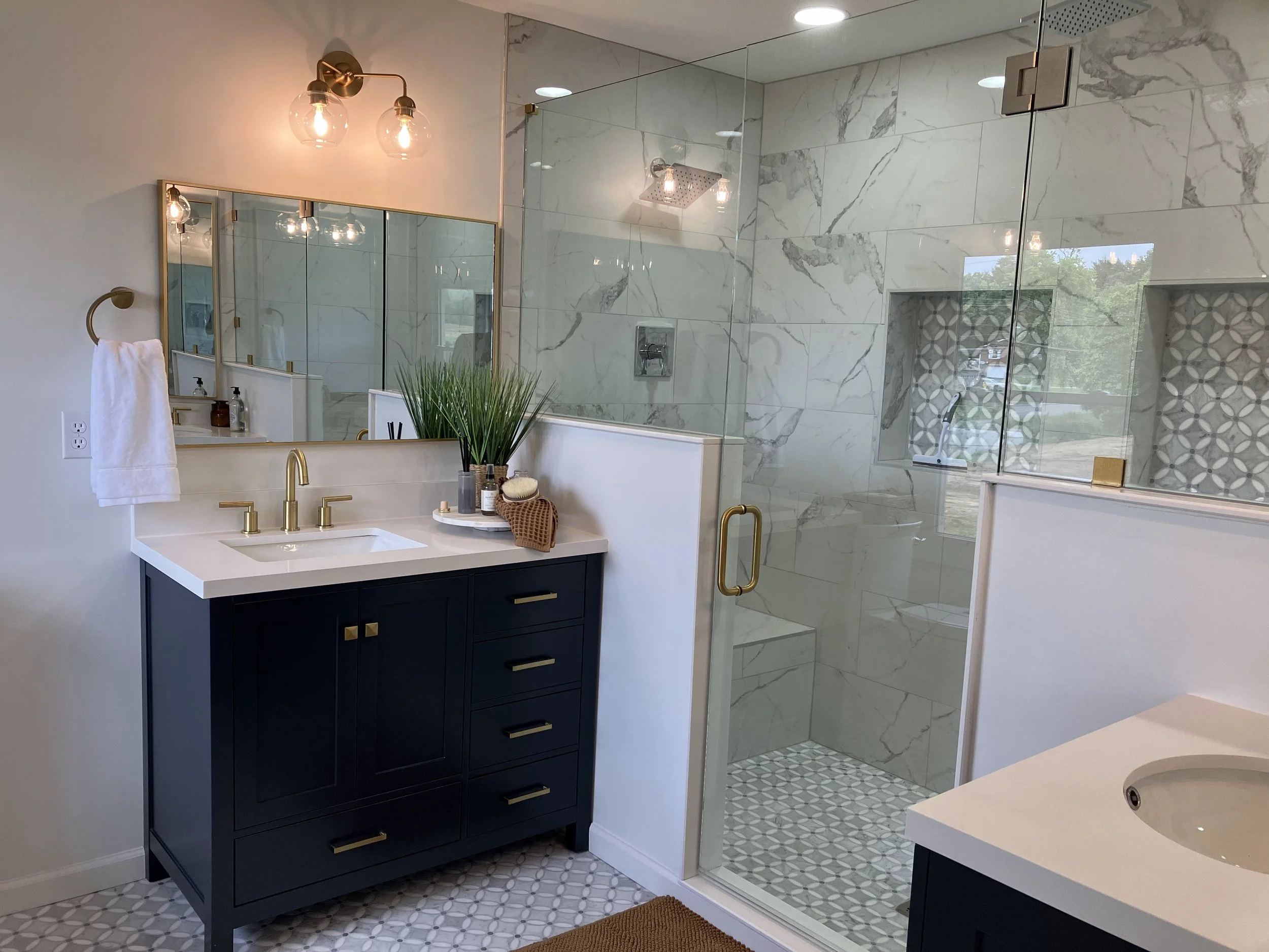 Modern bathroom with navy vanity, gold fixtures, and glass shower.