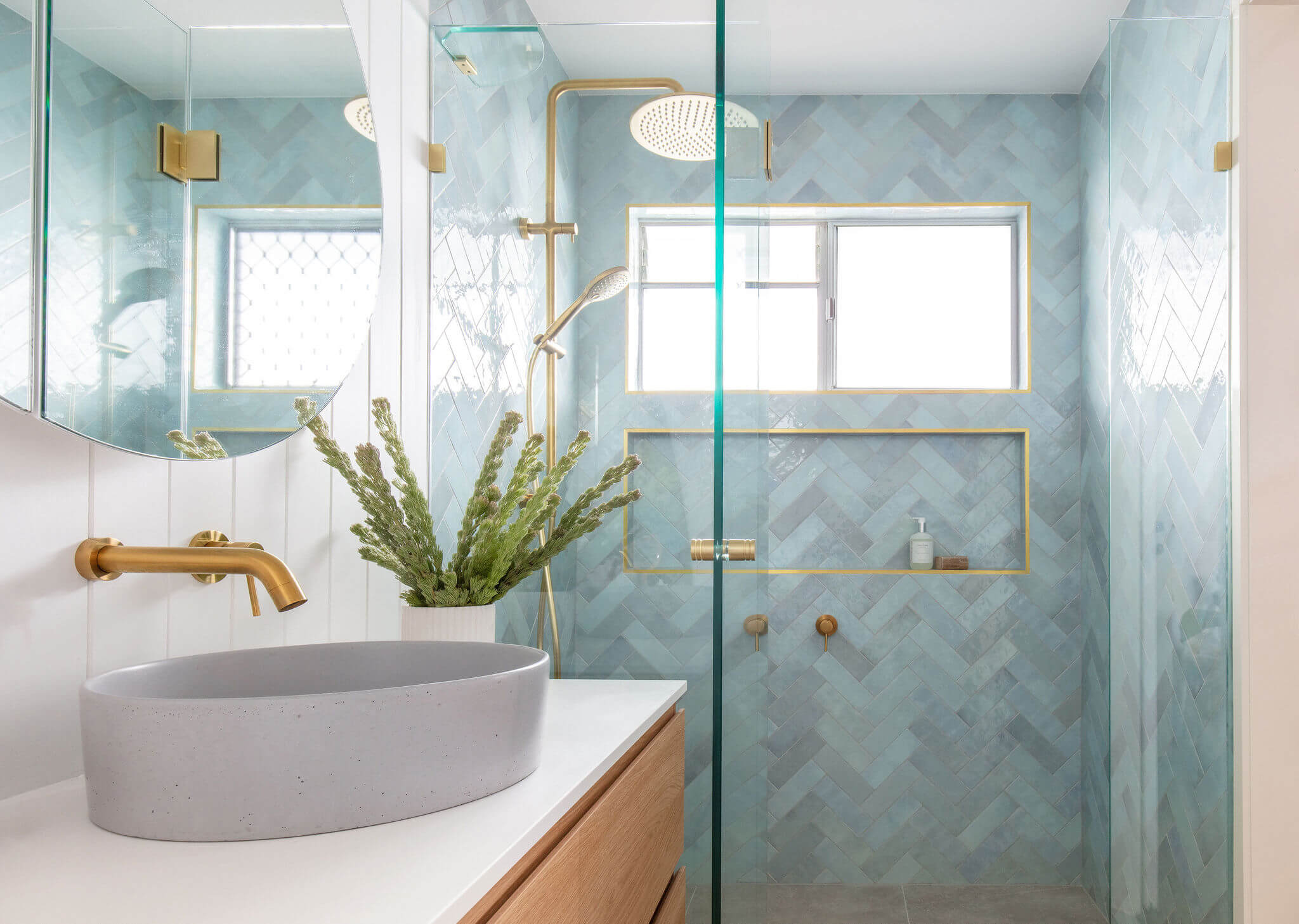 Modern bathroom with blue herringbone tiles, gold fixtures, and a concrete vessel sink.