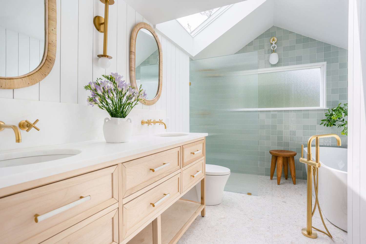 Bright modern bathroom with light wood vanity and gold fixtures.