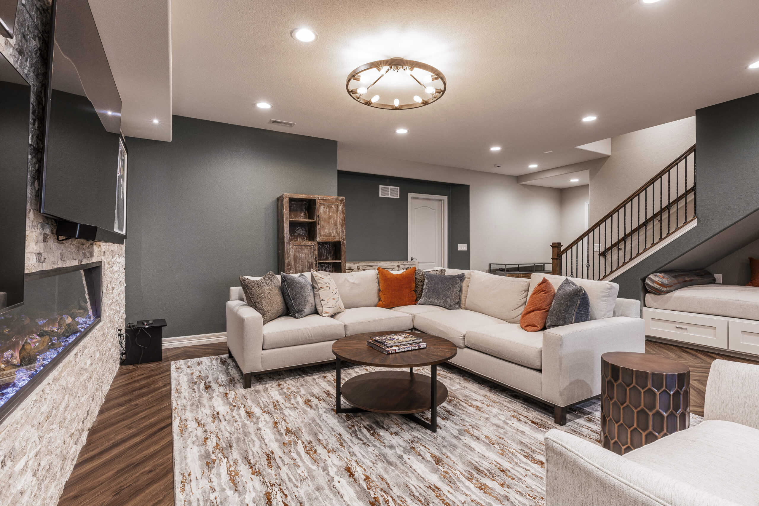 Finished basement featuring a large sectional sofa, modern fireplace, flat-screen TV, wood flooring, and a stylish staircase.