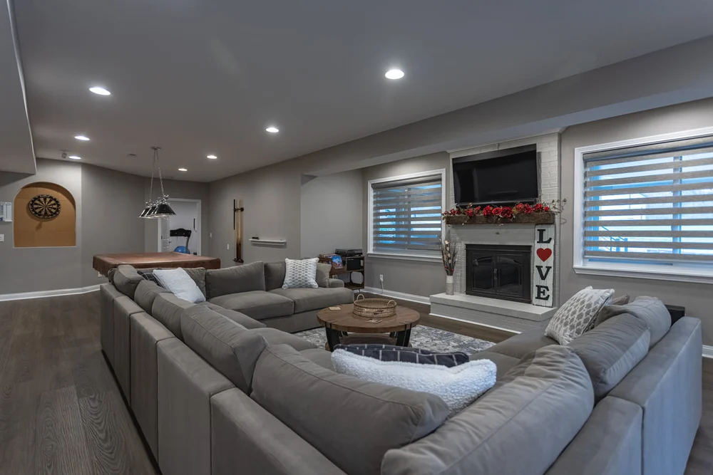 A cozy, modern finished basement with a large sectional, fireplace, TV, and game area.