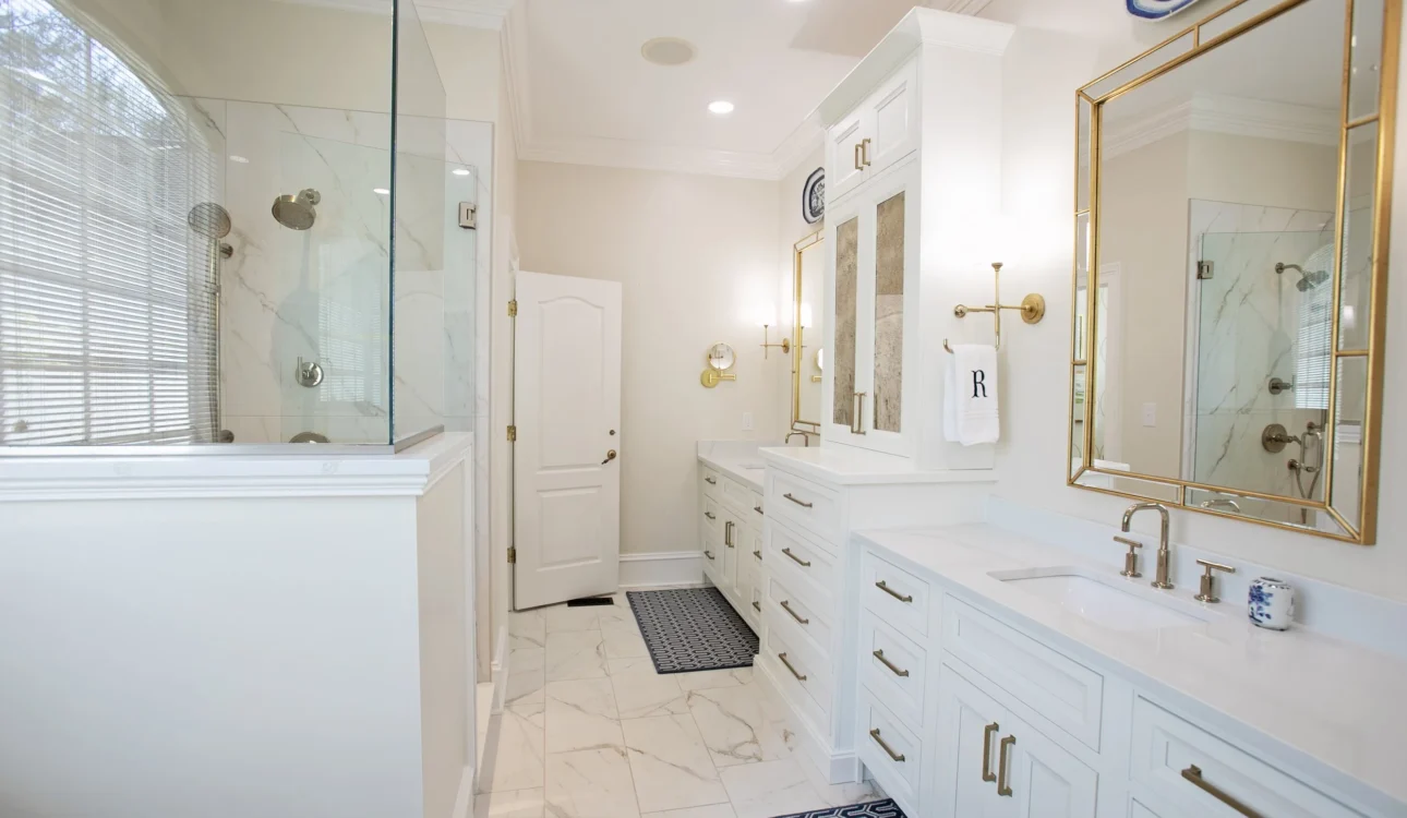 Elegant white bathroom with glass shower, double vanities, and gold accents.