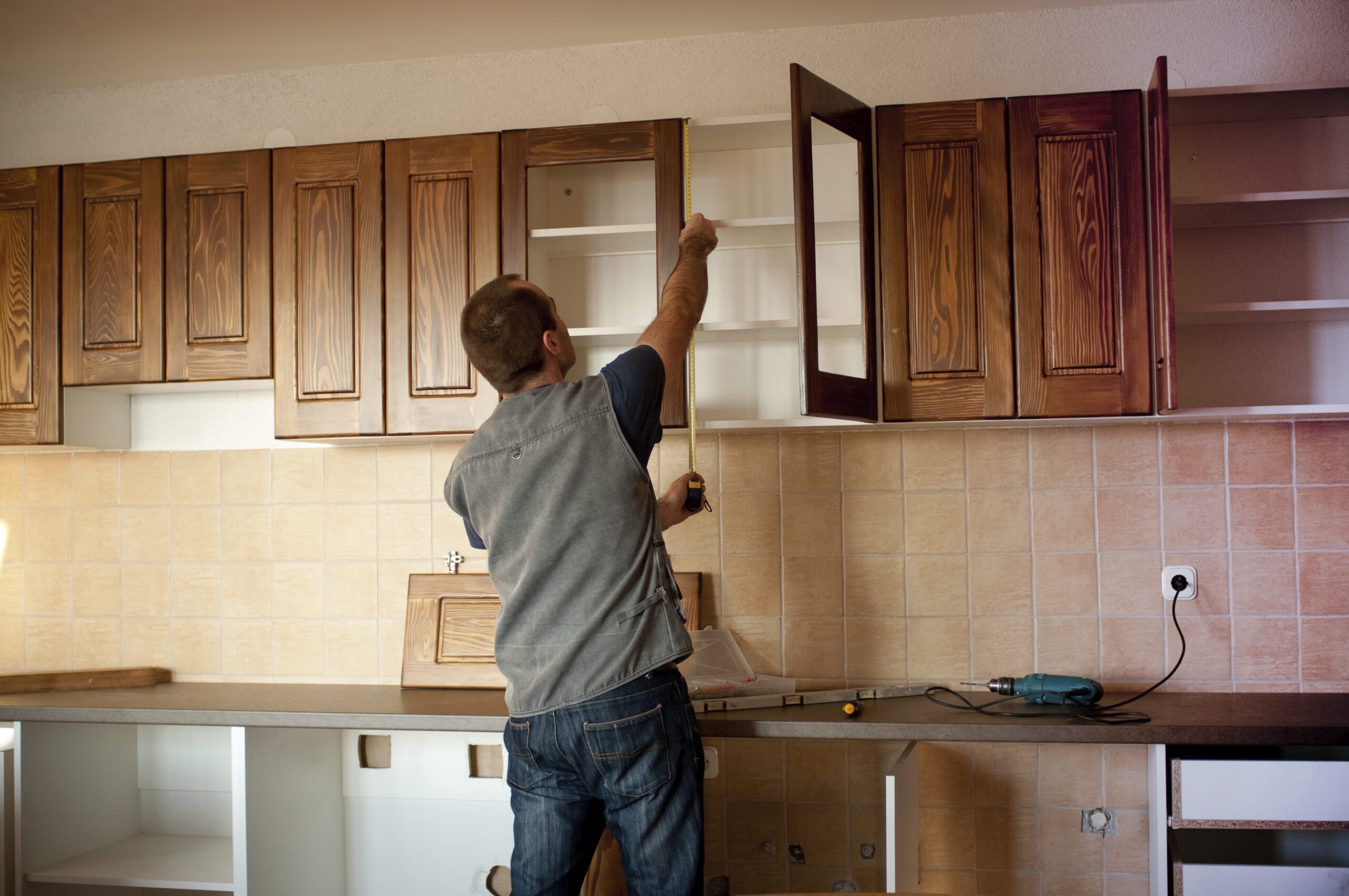 Man measuring upper kitchen cabinets during a kitchen remodel.
