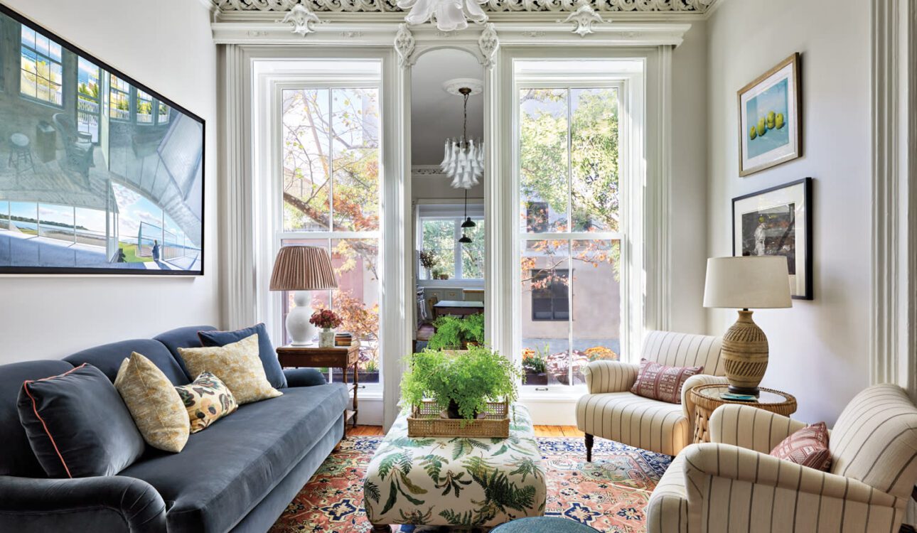 Eclectic living room with navy sofa, patterned rug, striped armchairs, large windows, and ornate crown molding.