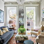 Eclectic living room with navy sofa, patterned rug, striped armchairs, large windows, and ornate crown molding.