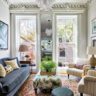Eclectic living room with navy sofa, patterned rug, striped armchairs, large windows, and ornate crown molding.
