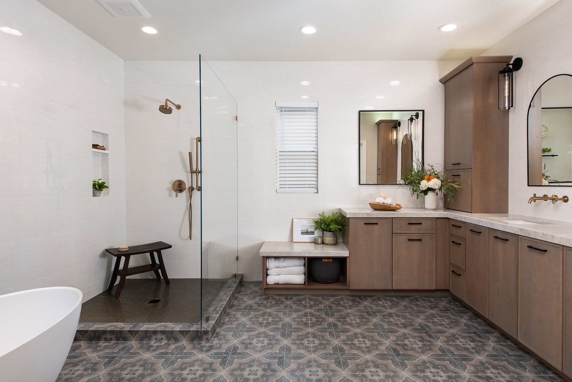 Spacious modern bathroom with glass walk-in shower, wooden cabinets, freestanding tub, and patterned tile floor.