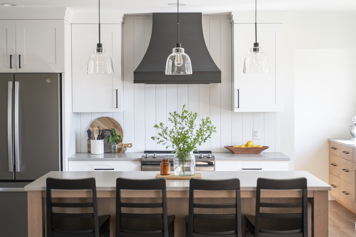 Modern kitchen with white cabinets, black range hood, and wooden island seating.