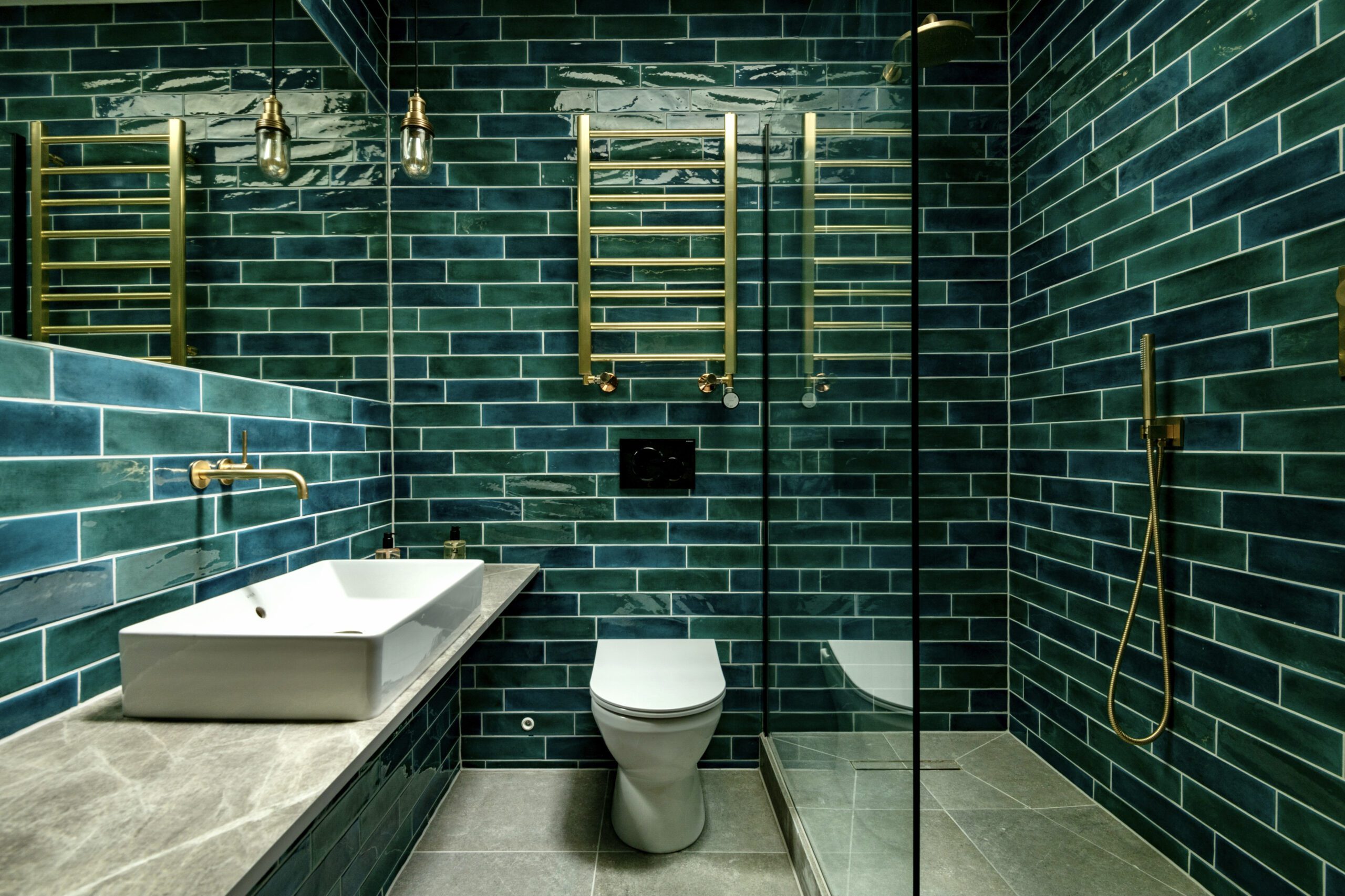 Modern bathroom with teal subway tiles and gold fixtures.