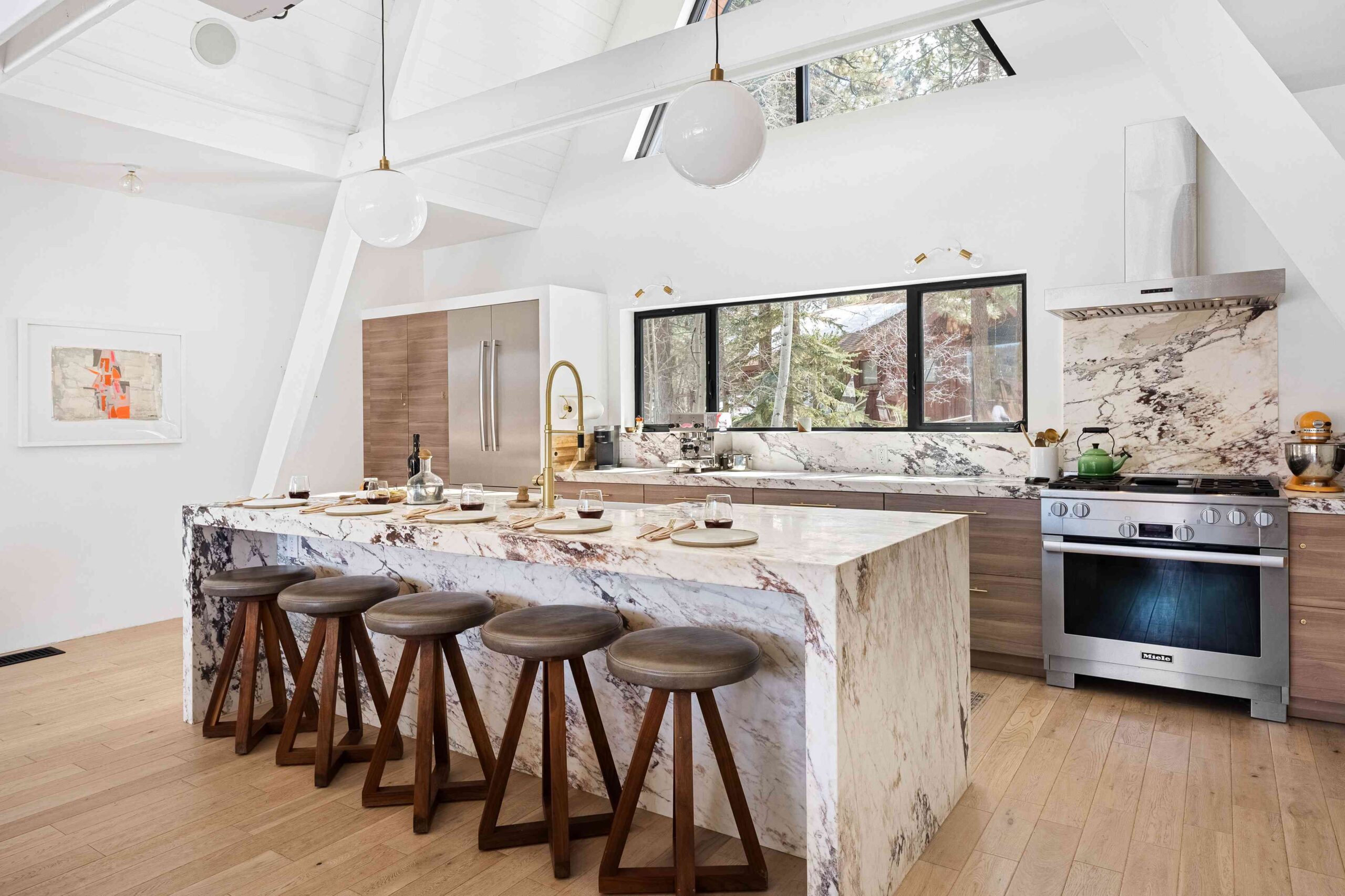 Modern kitchen with marble island, wooden stools, and large windows.