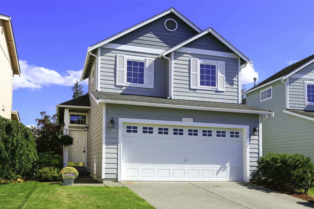 A light gray modern two-story house with a white garage door and manicured front yard.