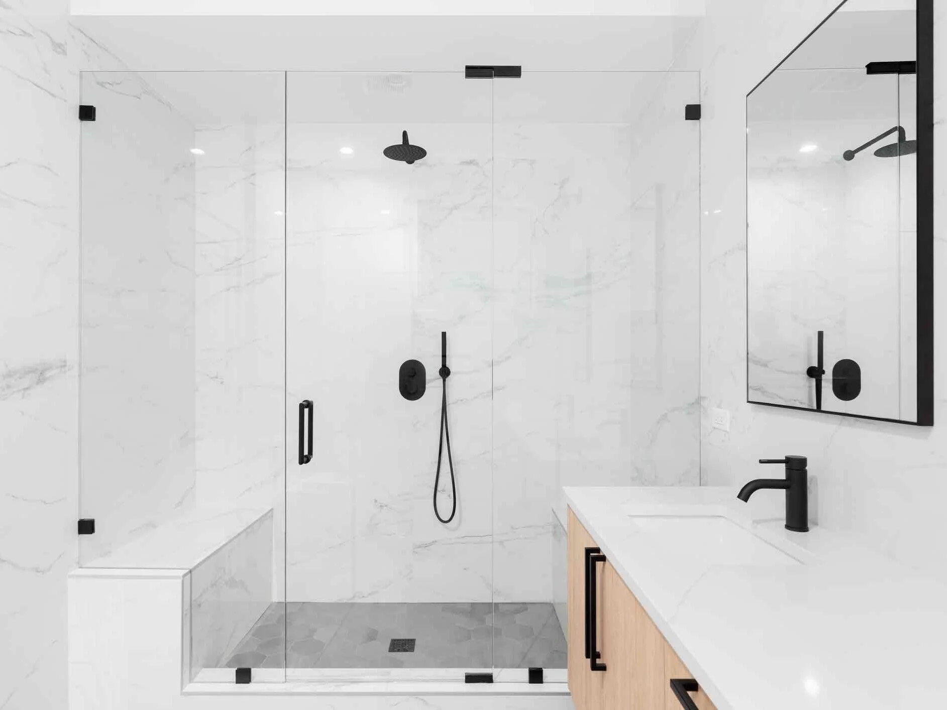 Modern walk-in shower with glass enclosure, black fixtures, and white marble walls.
