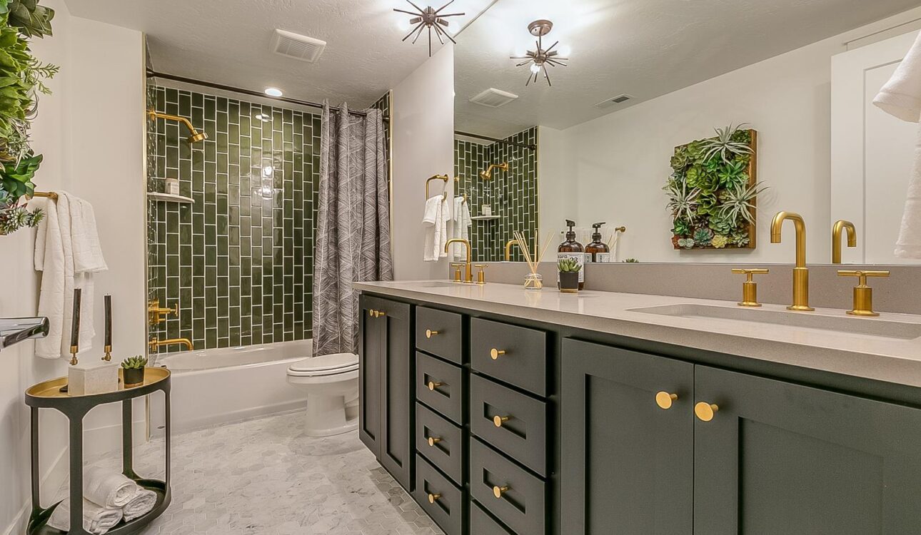 Elegant bathroom featuring a green vertical subway tile shower, black double vanity with gold hardware, large mirror, and modern lighting.
