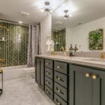 Elegant bathroom featuring a green vertical subway tile shower, black double vanity with gold hardware, large mirror, and modern lighting.