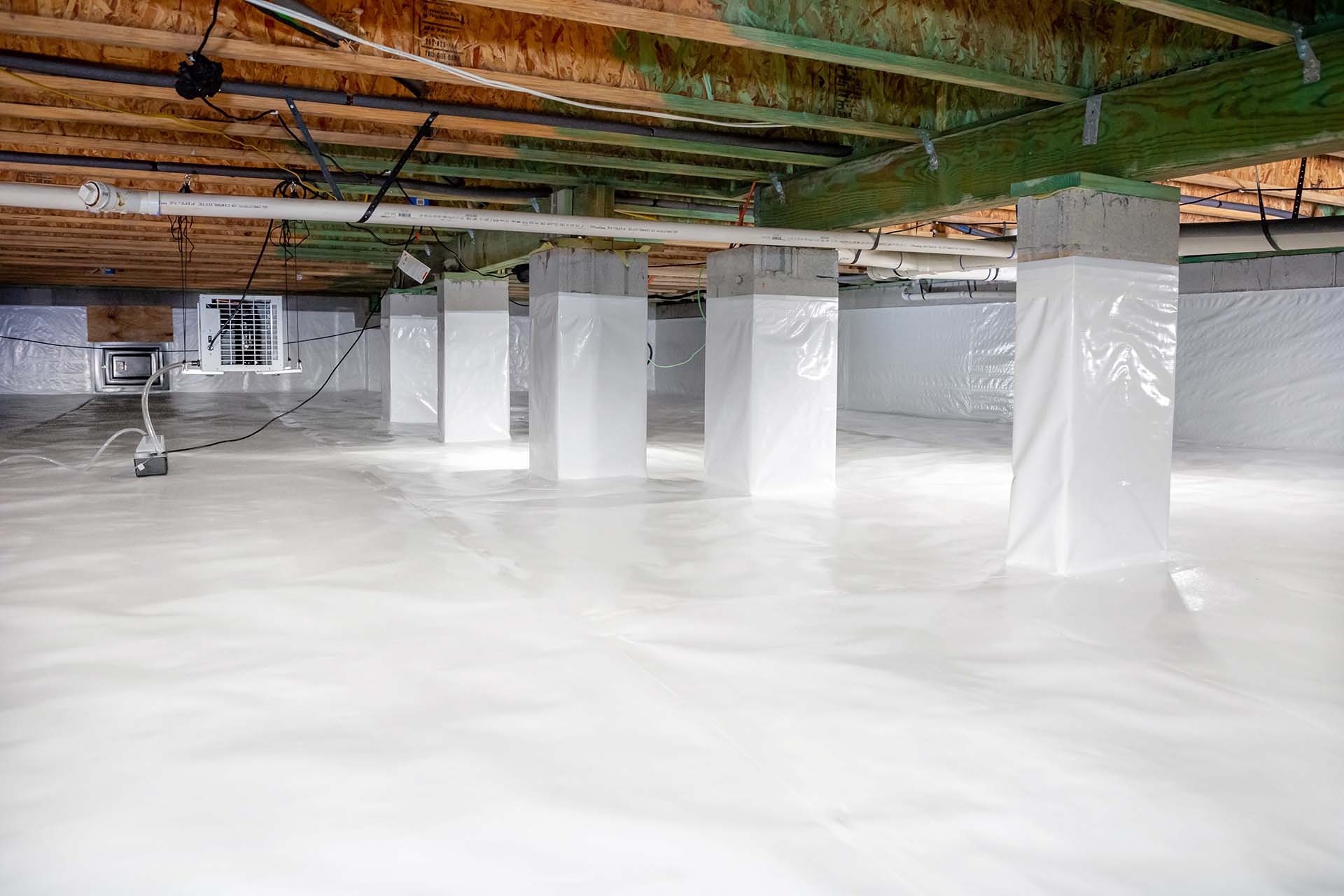 A clean, encapsulated crawl space with white vapor barriers covering the floor, walls, and support piers.